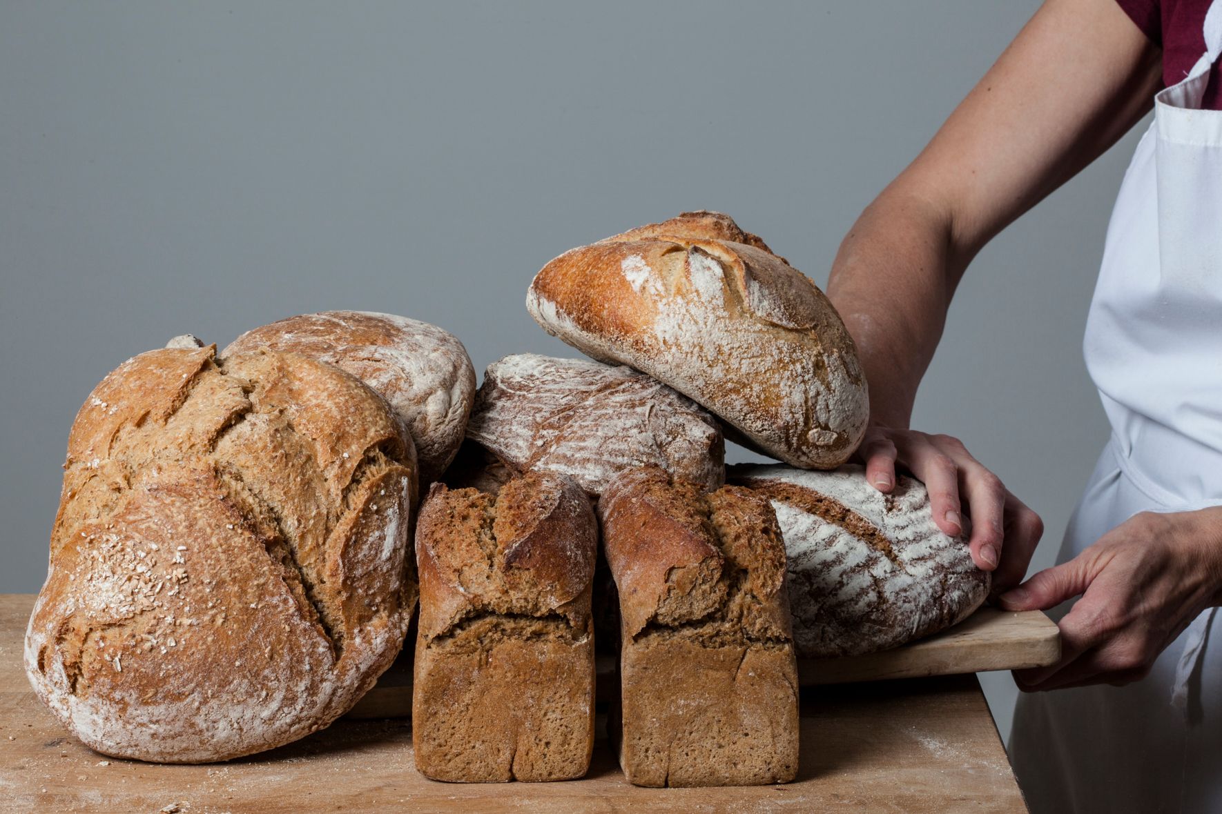 Various loaves of bread on a wooden board, held by a person in an apron.