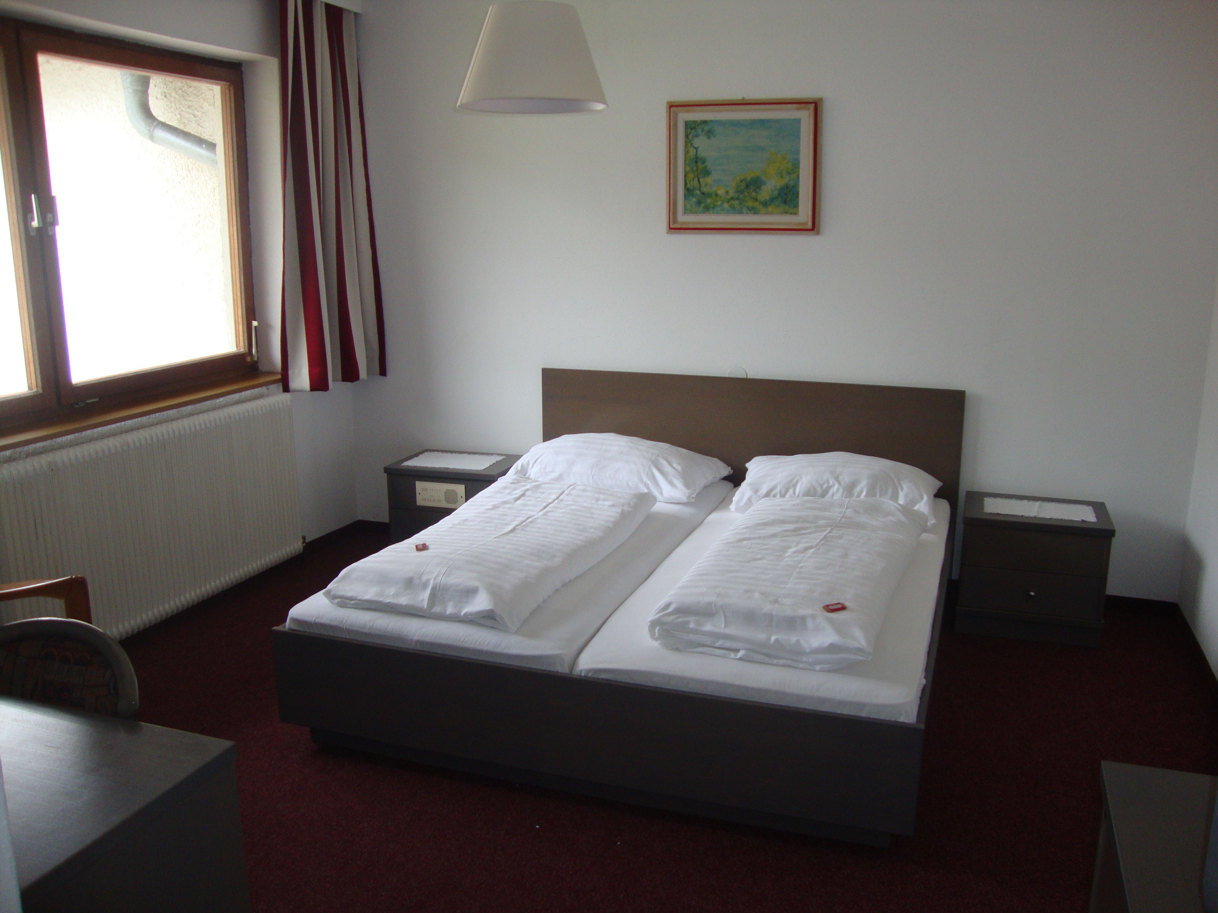 A simply furnished hotel room with a double bed, bedside tables and a window with curtains.