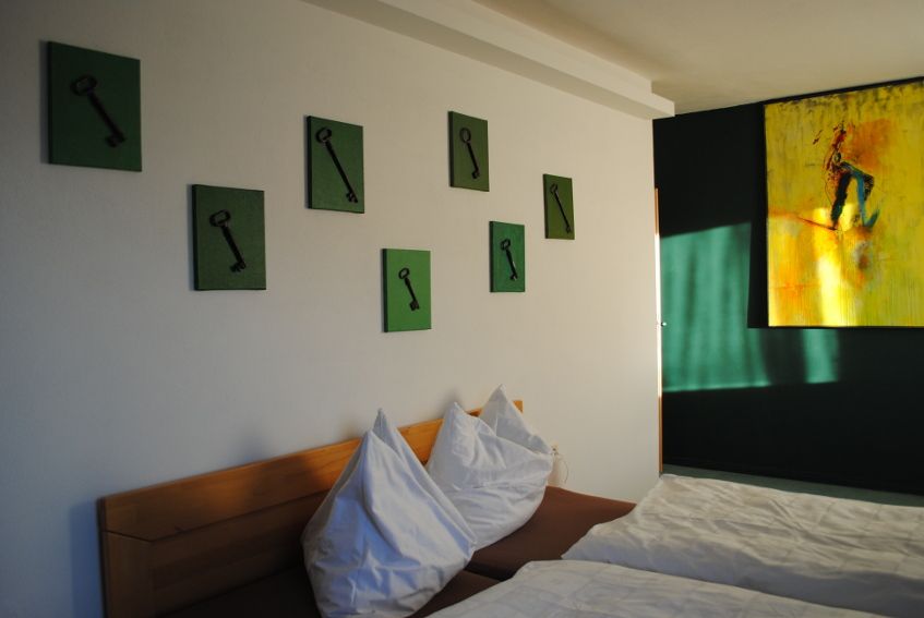 A room with two beds, green pictures of keys on the wall and a yellow painting.