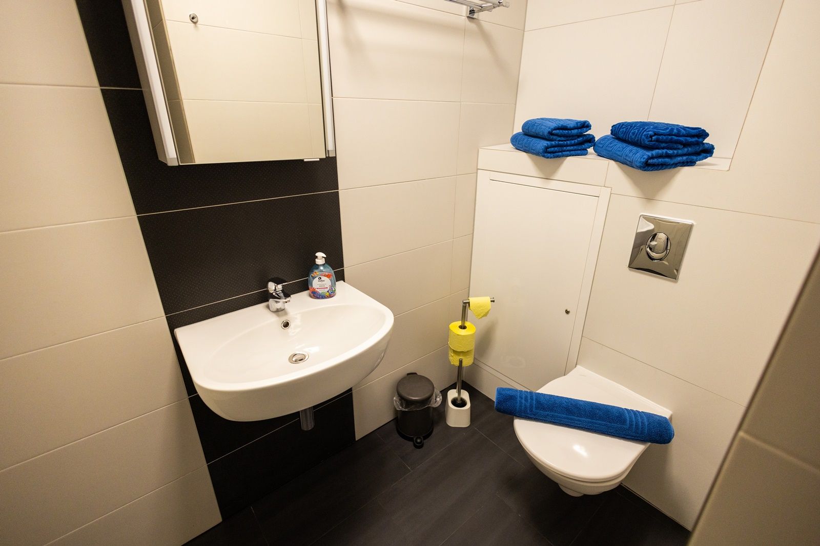 Small bathroom with washbasin, toilet, blue towels and yellow toilet paper.