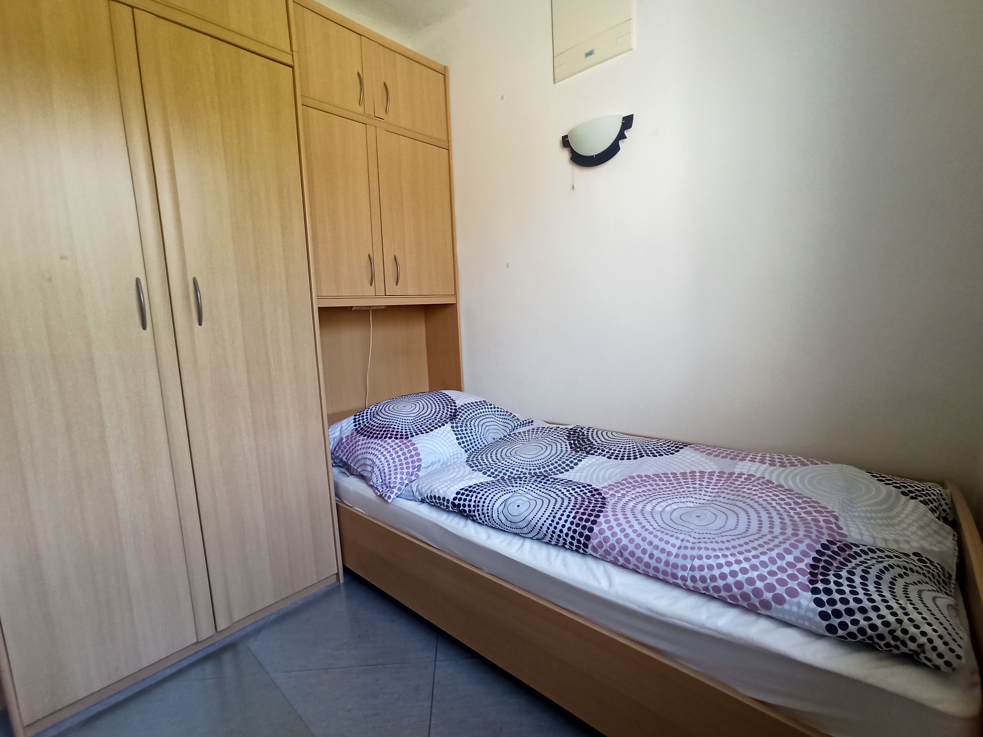 A simple bedroom with a single bed and a large wooden wardrobe.