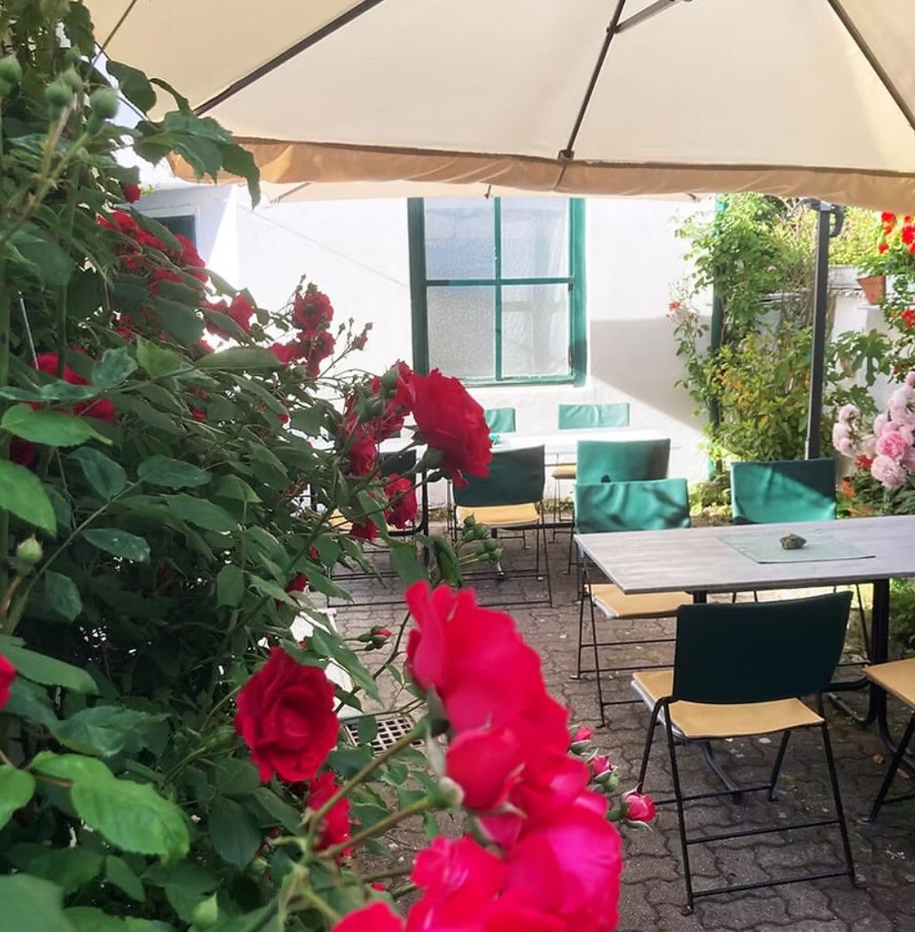 A cozy outdoor area of a café with tables, chairs and red roses under a parasol.