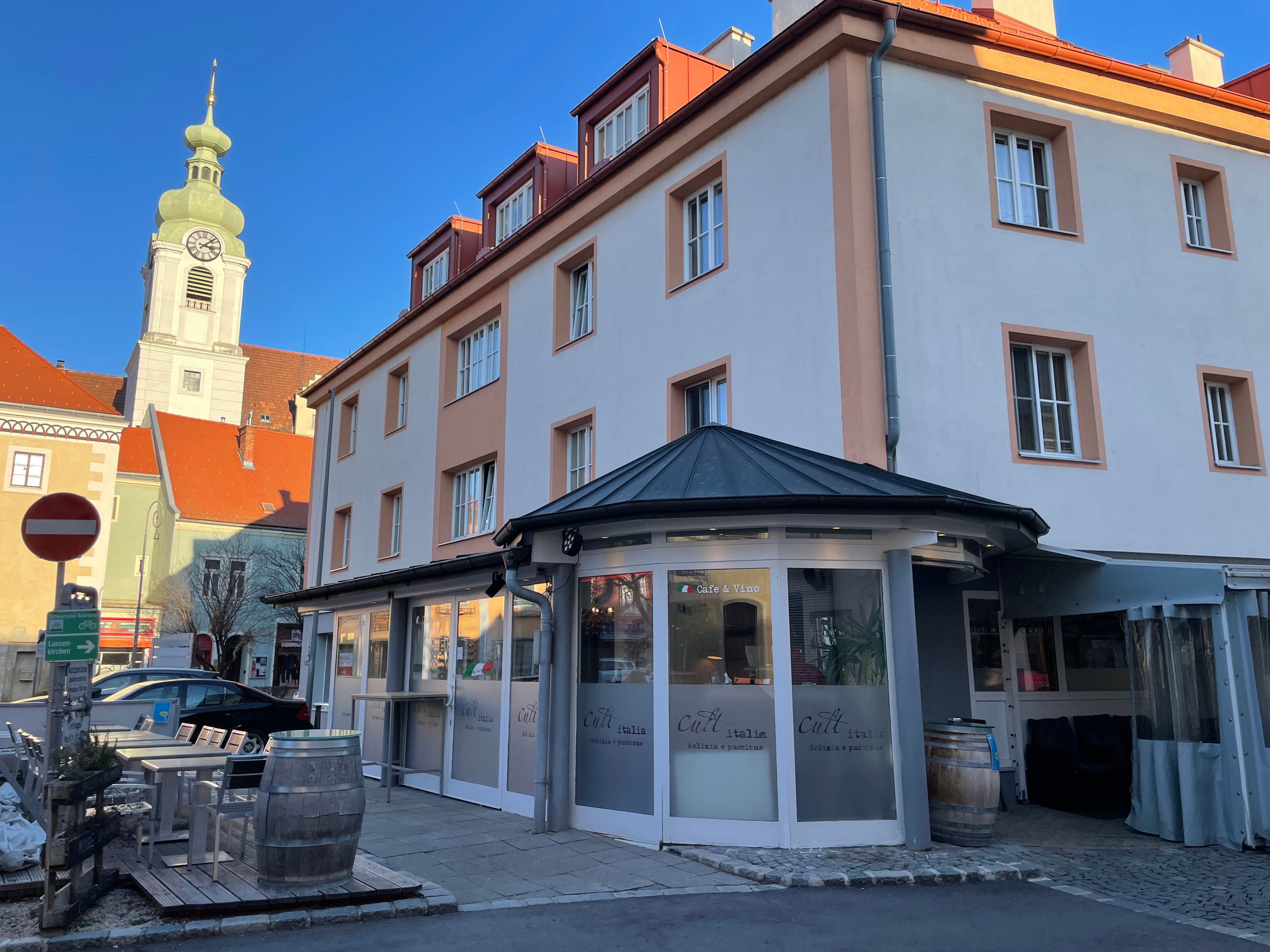 Exterior view of a restaurant with the inscription 'Cult Italia' and a church tower in the background.