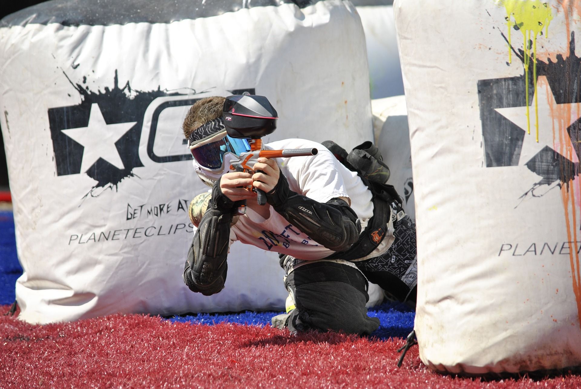 A paintball player in protective clothing aims a paintball gun behind an inflatable cover.