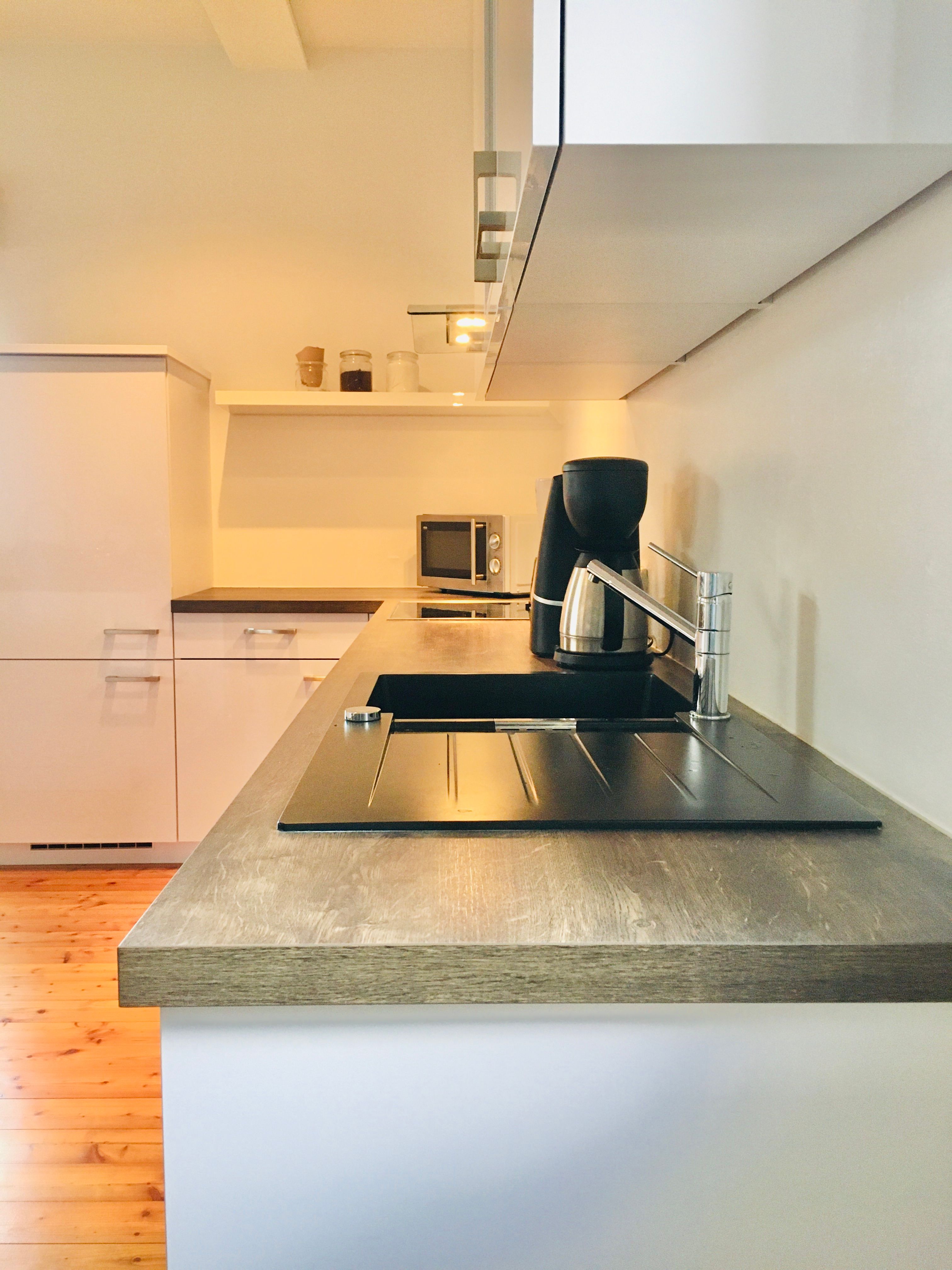 Modern kitchen with wooden worktop, sink, coffee machine and microwave.
