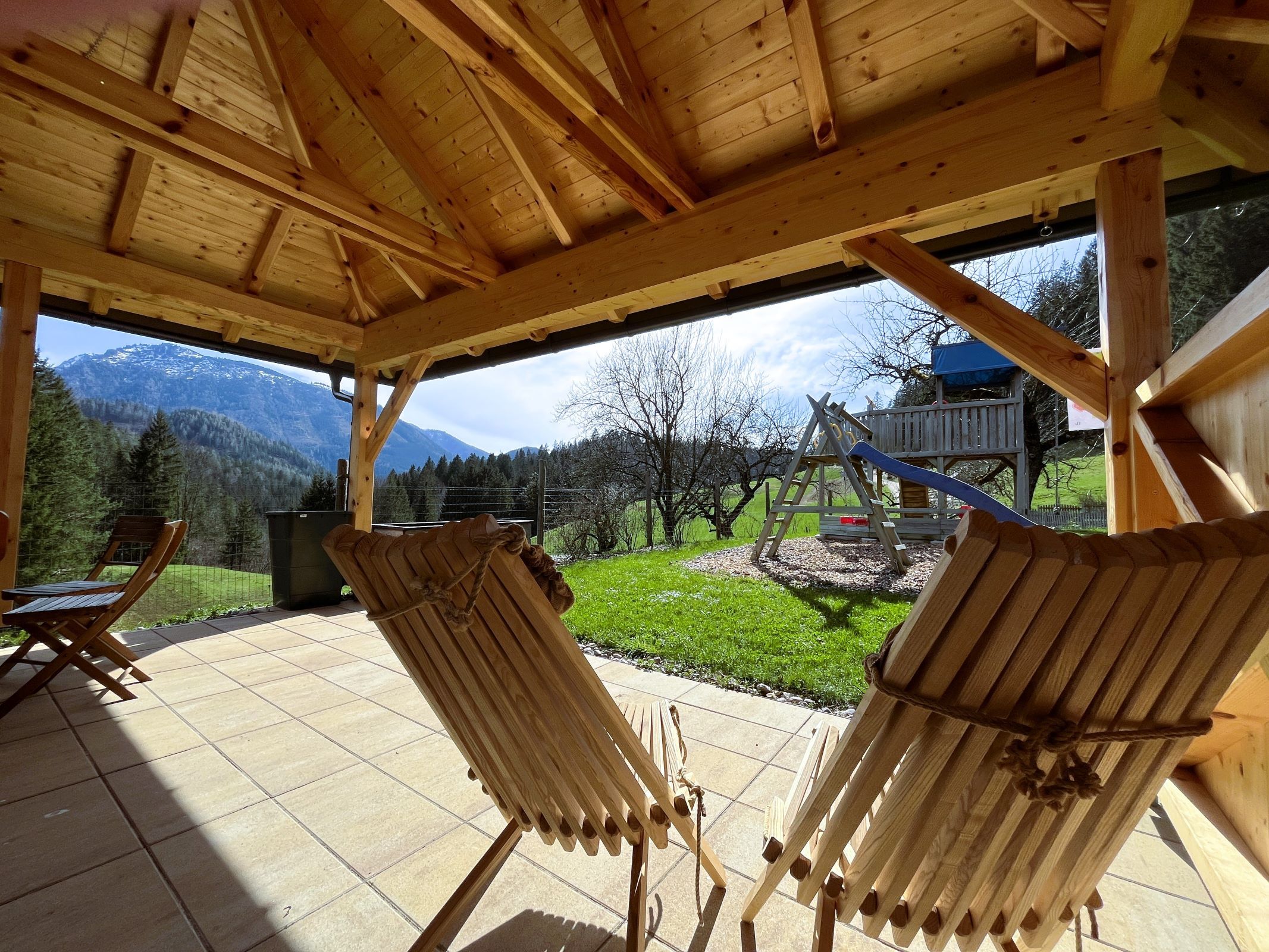 View from a wooden pavilion of a mountain landscape with a swing and slide in the garden.