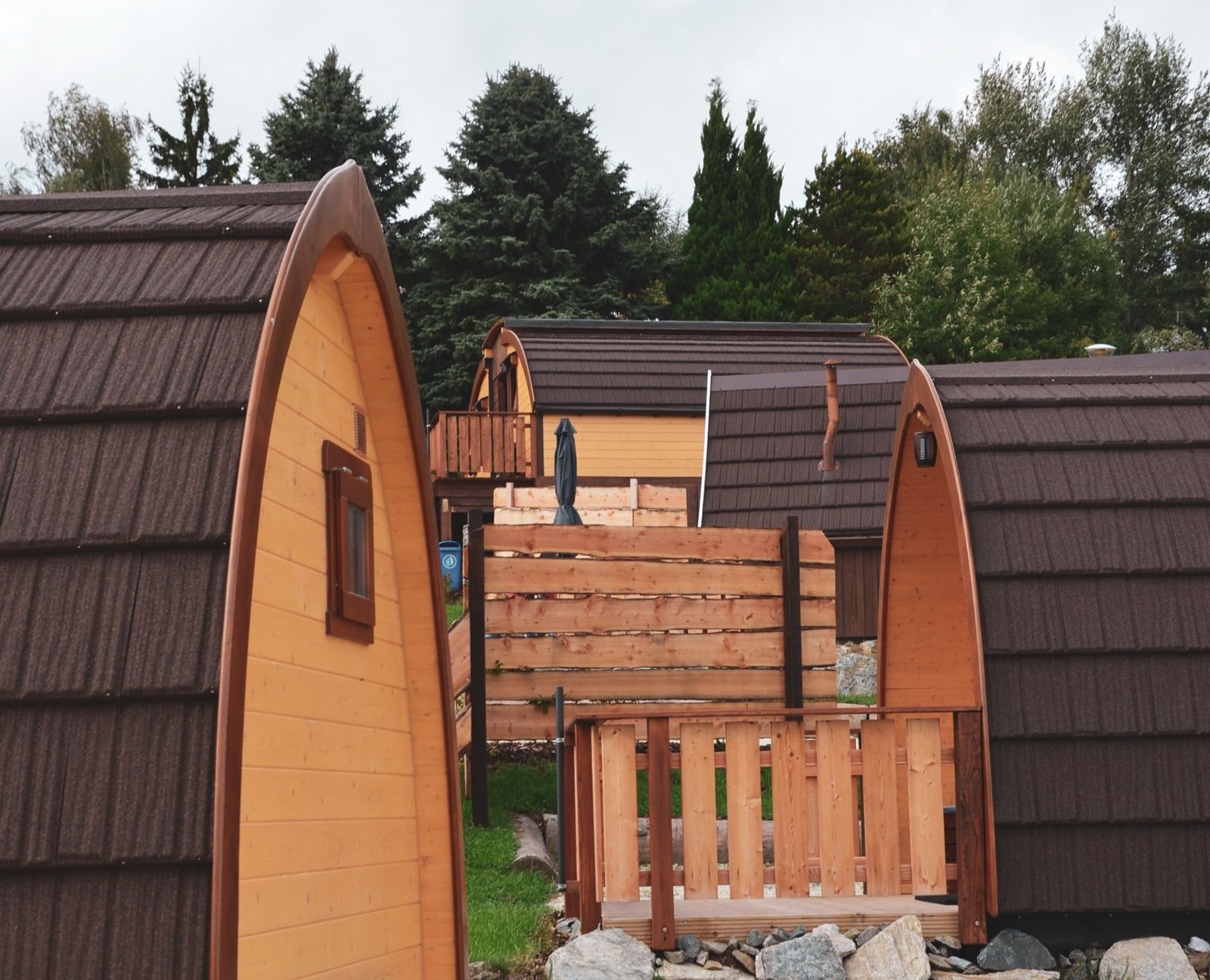 Several wooden glamping huts with brown roofs in a wooded area.