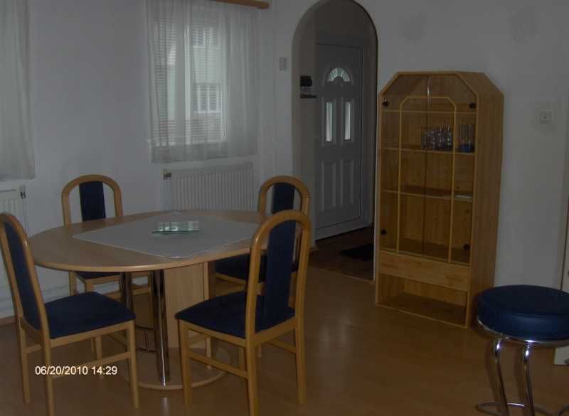 Dining area with round table, four chairs and a wooden shelf in a bright room.
