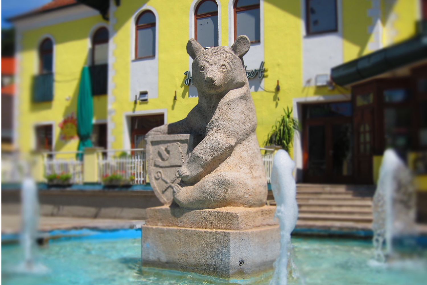 Stone bear sculpture with coat of arms in a fountain in front of a yellow building.