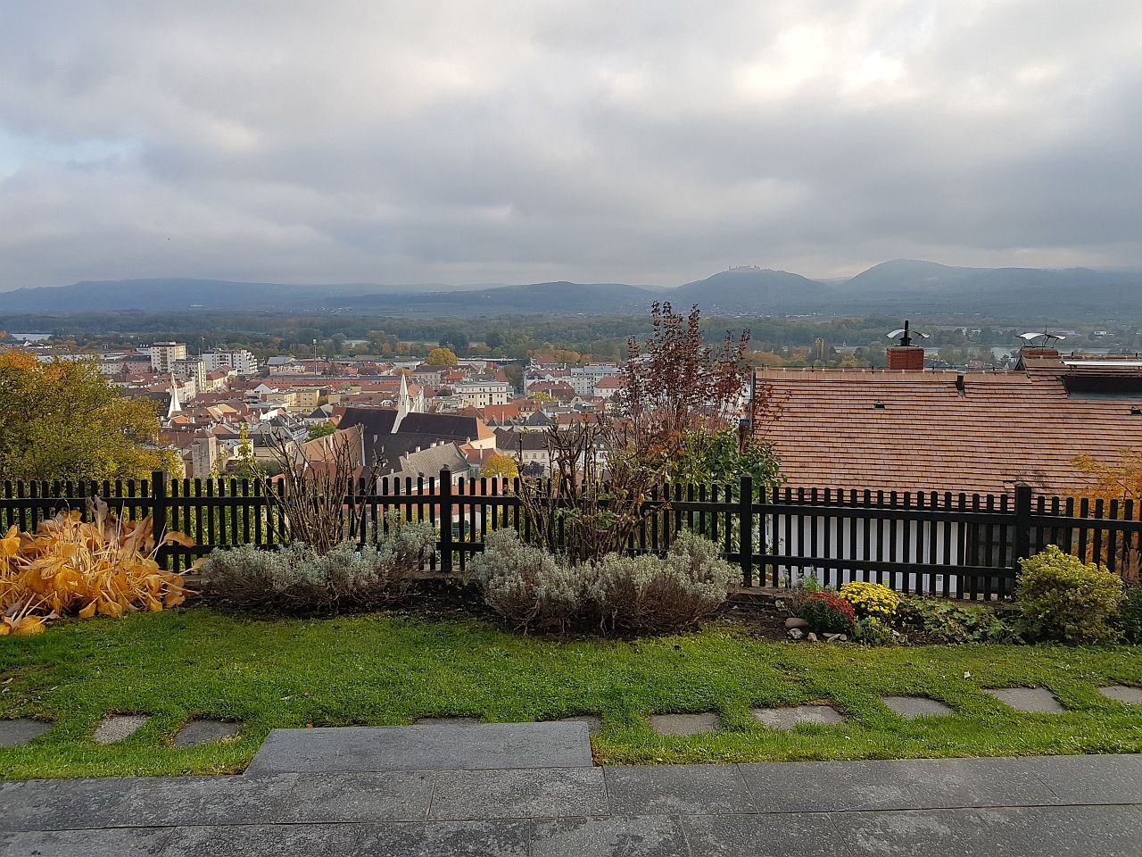 View over the town of Krems with houses, hills and a cloudy sky in the background.