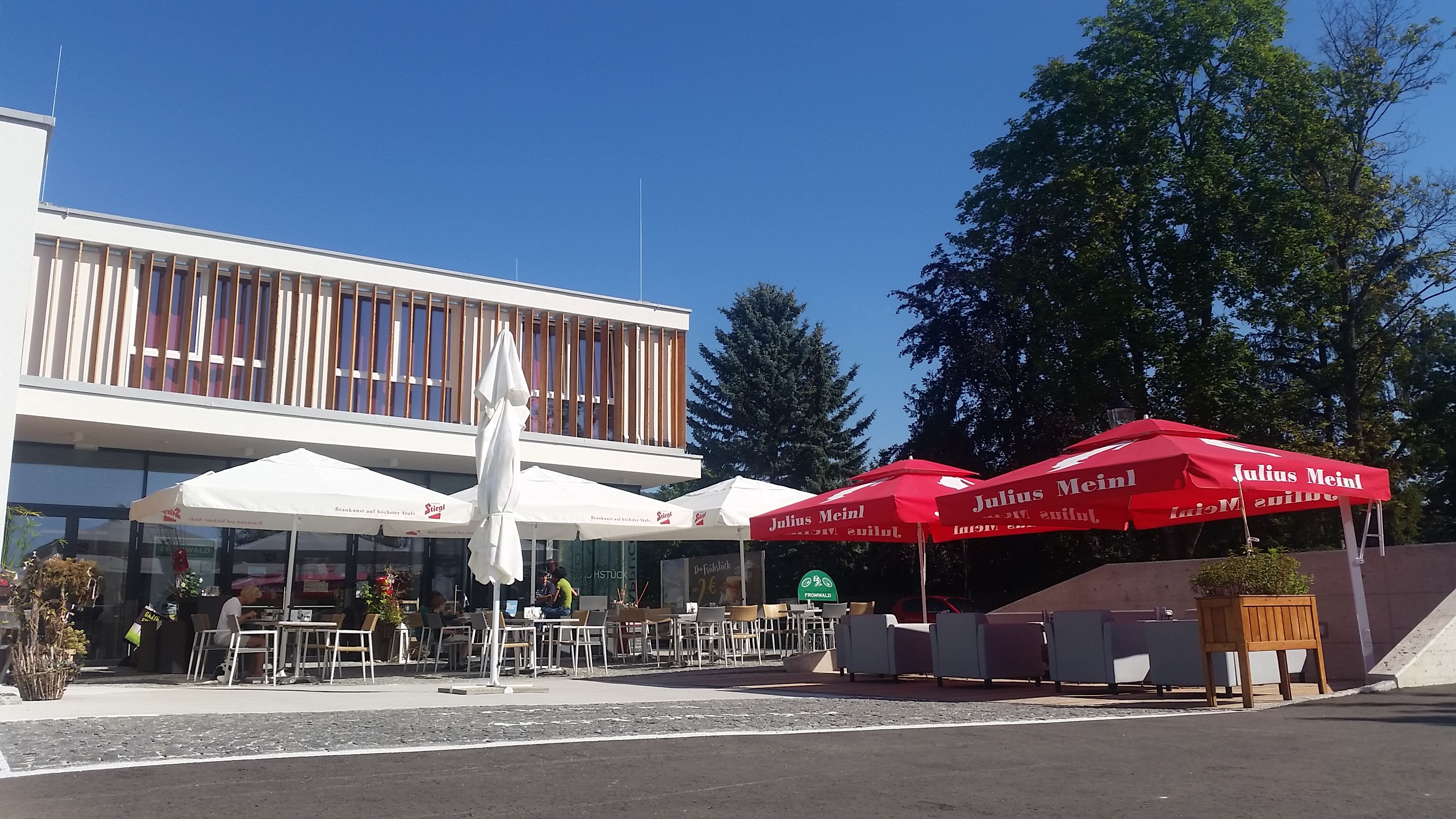 A modern guest garden with parasols and seating in front of a building in sunny weather.