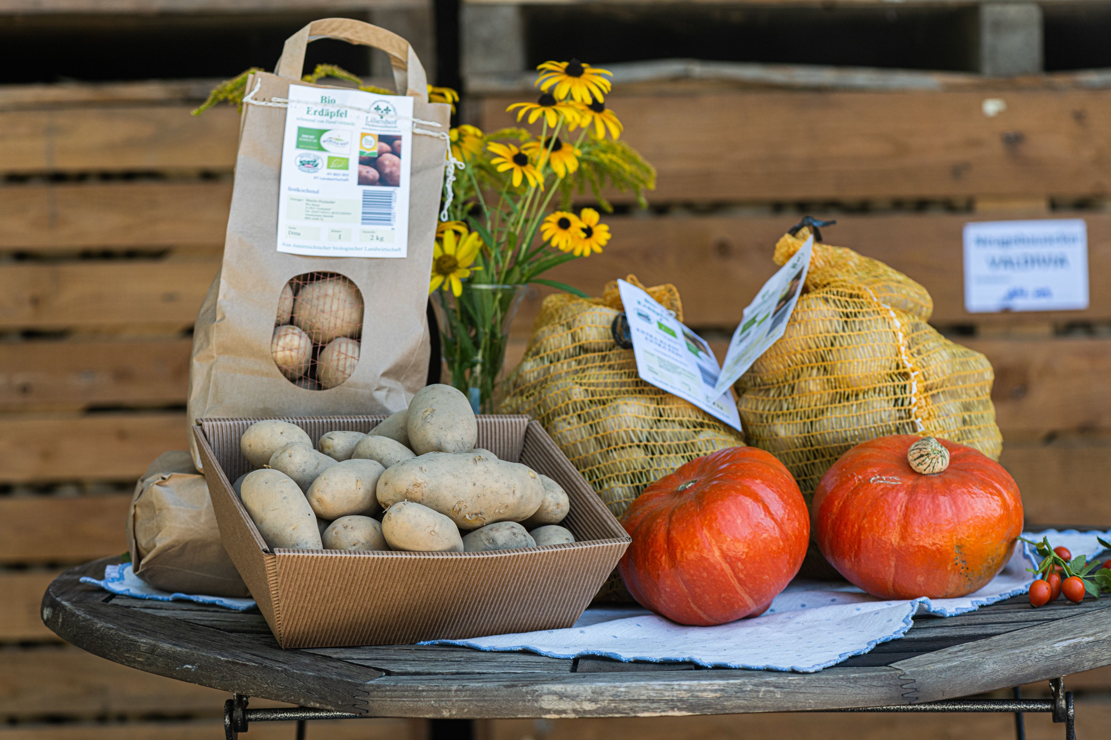 Potatoes, pumpkins and a vase of yellow flowers on a round wooden table.