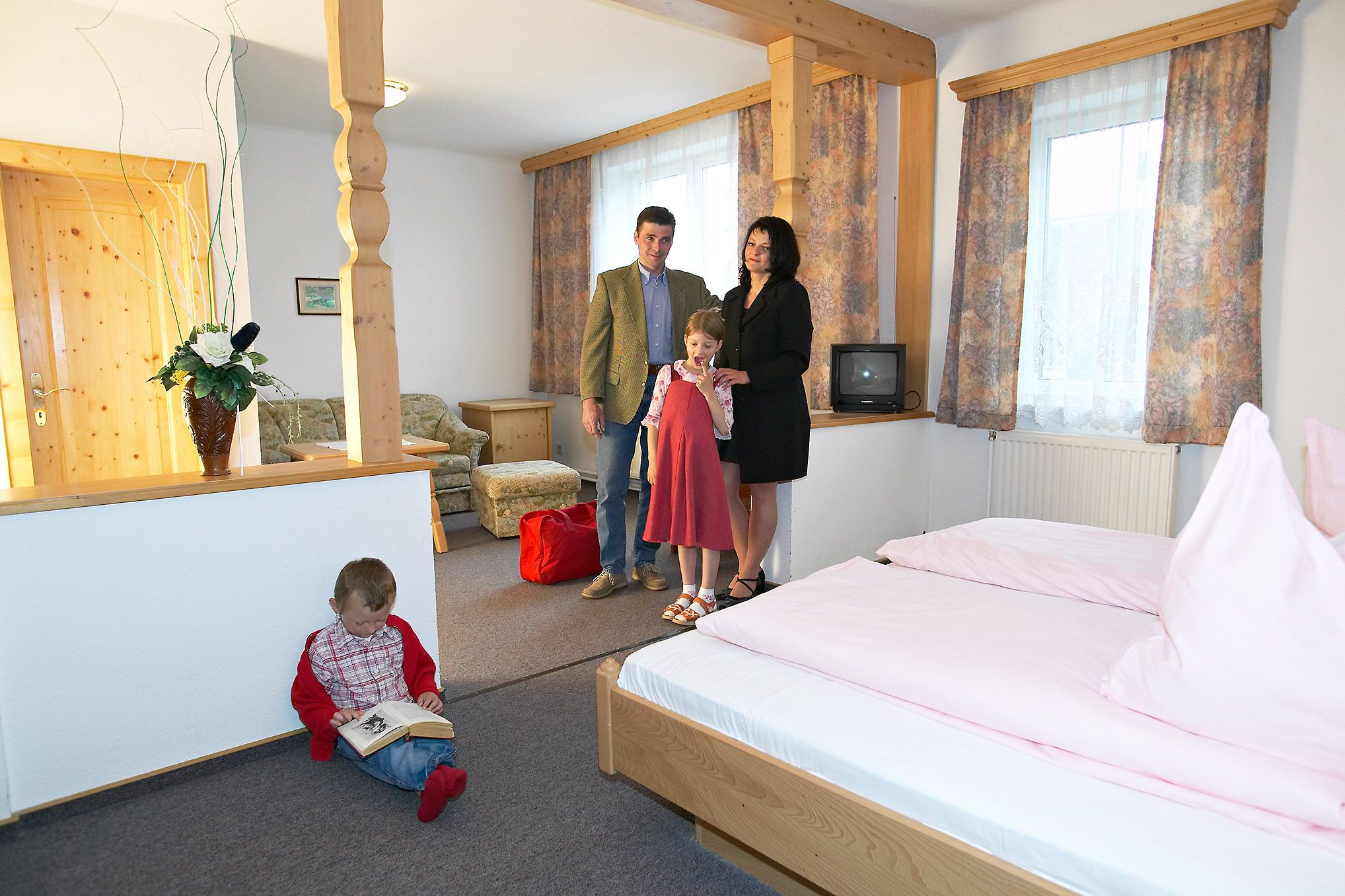 Family in a cozy hotel room with wooden furniture and pink bed linen.