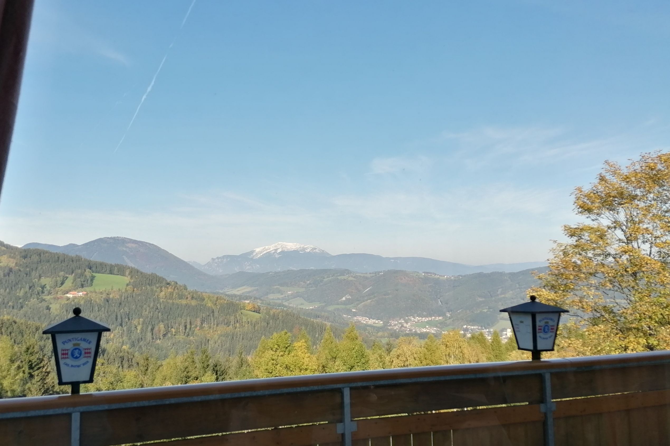 View from a restaurant balcony of a mountainous landscape with forest and a snow-capped peak in the background.