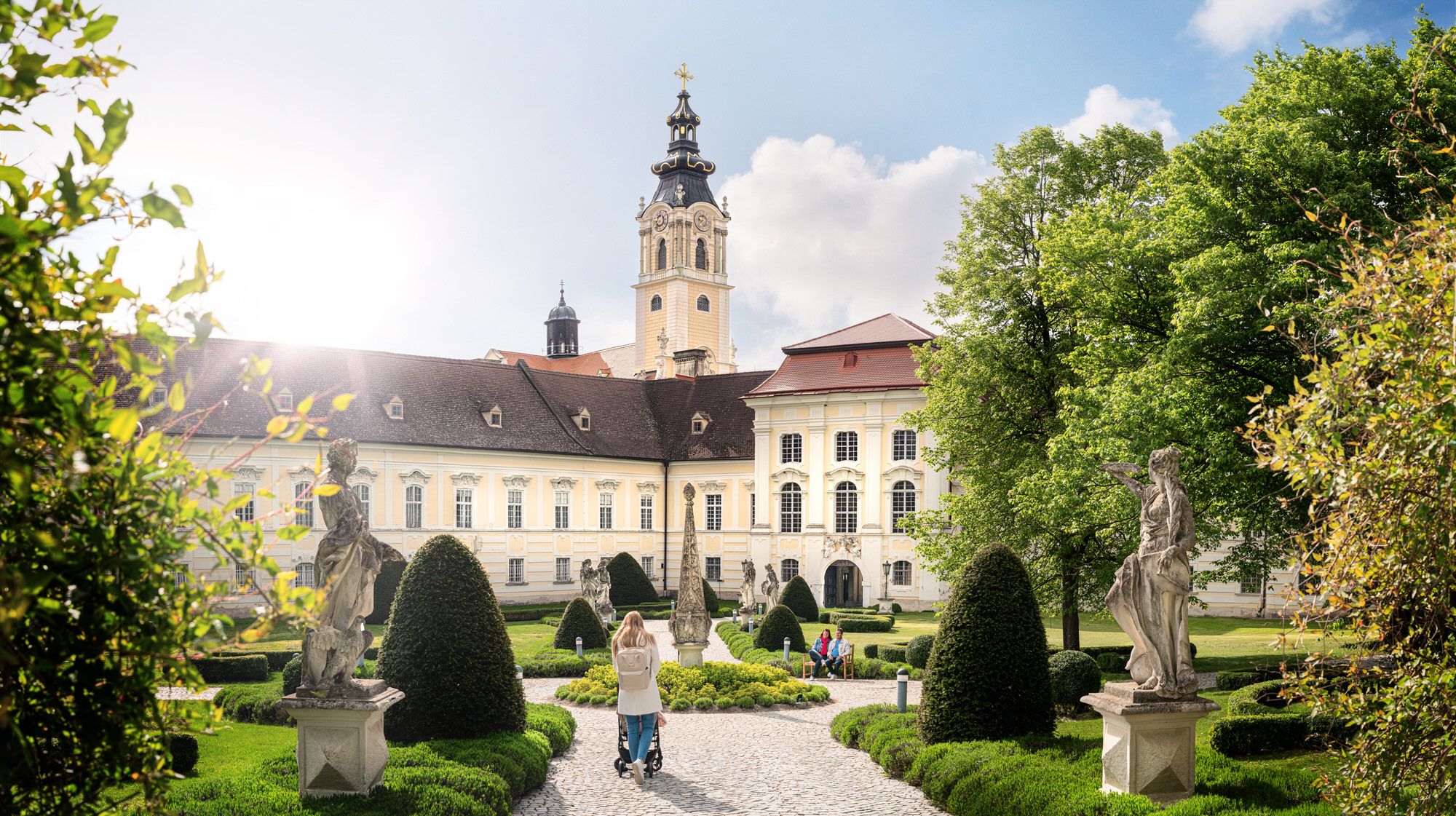 Baroque monastery with garden and statues in the foreground.