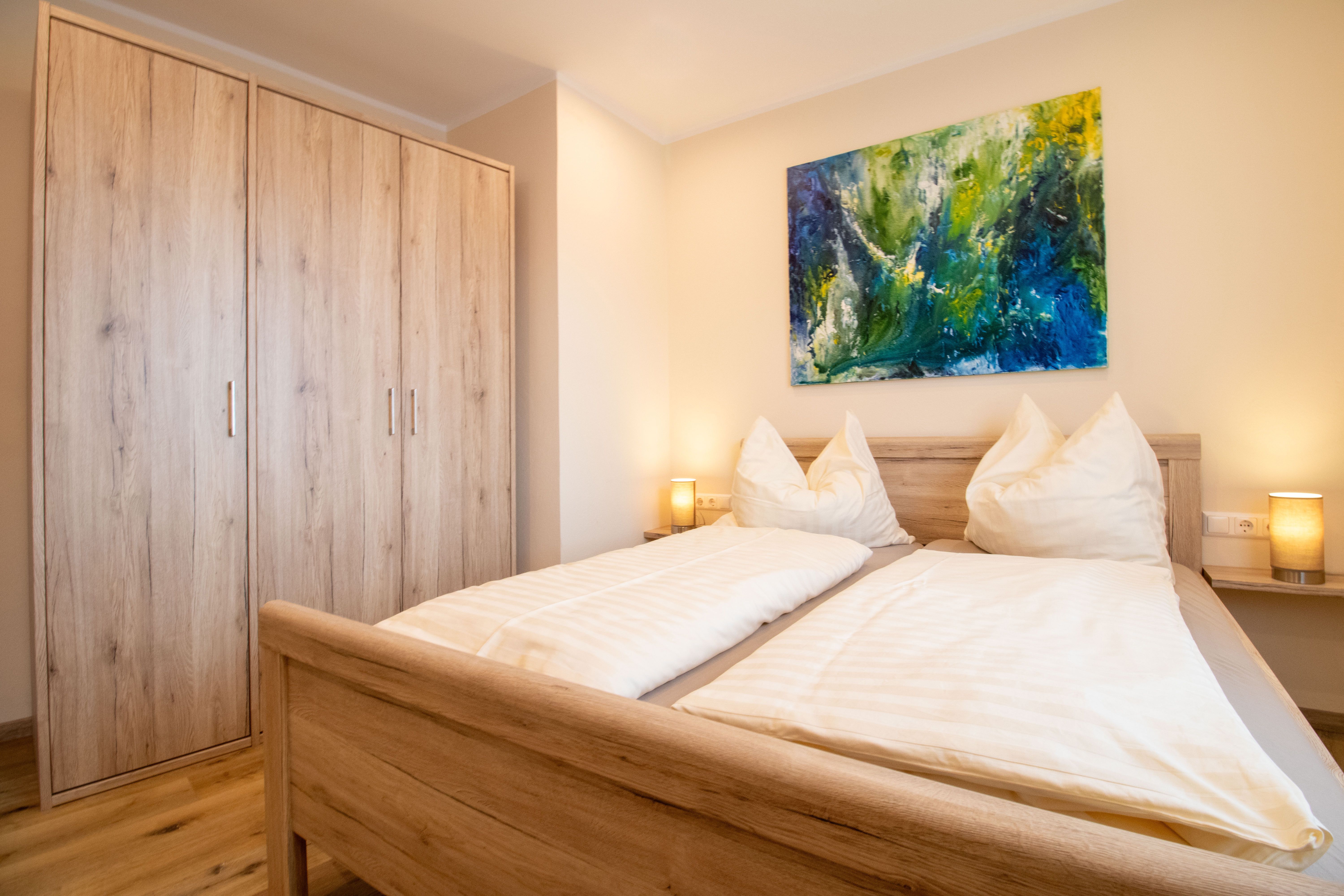 A cozy bedroom with a double bed, wooden furniture, and a colorful painting on the wall.