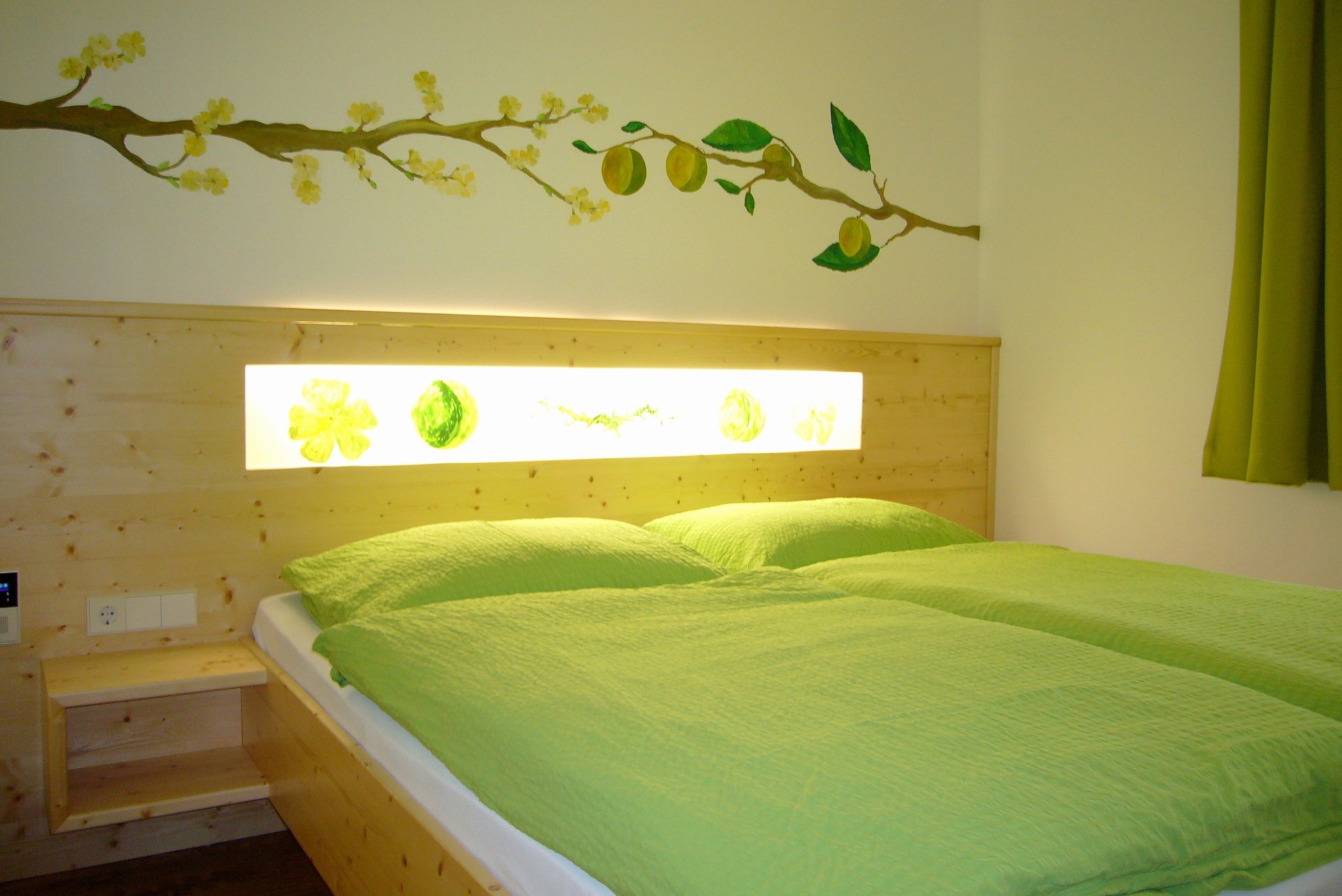 A cozy room with a double bed, green bed linen and a wall decoration with yellow flowers and fruits.
