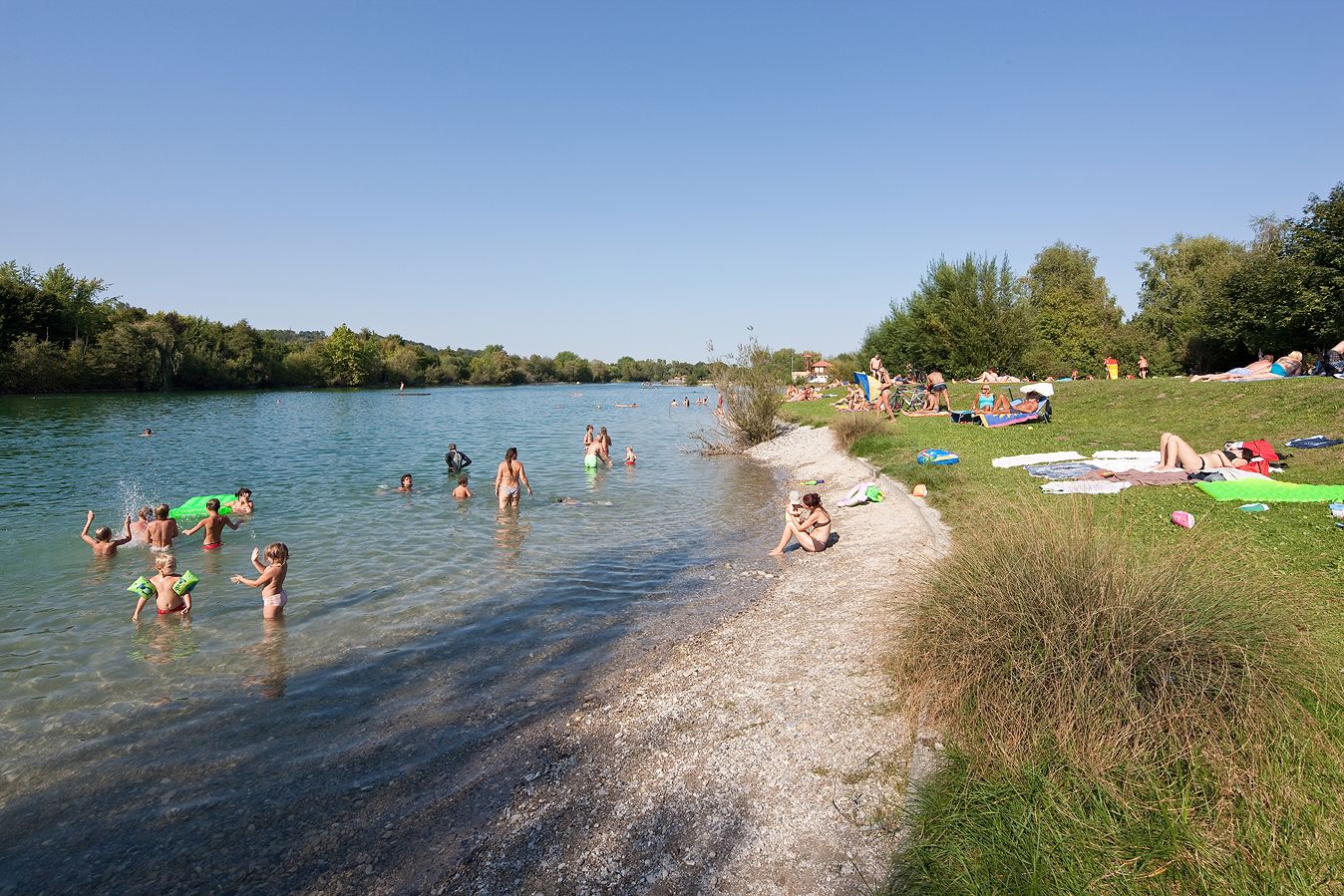 People swimming and relaxing at Lake Ratzersdorf on a sunny day.