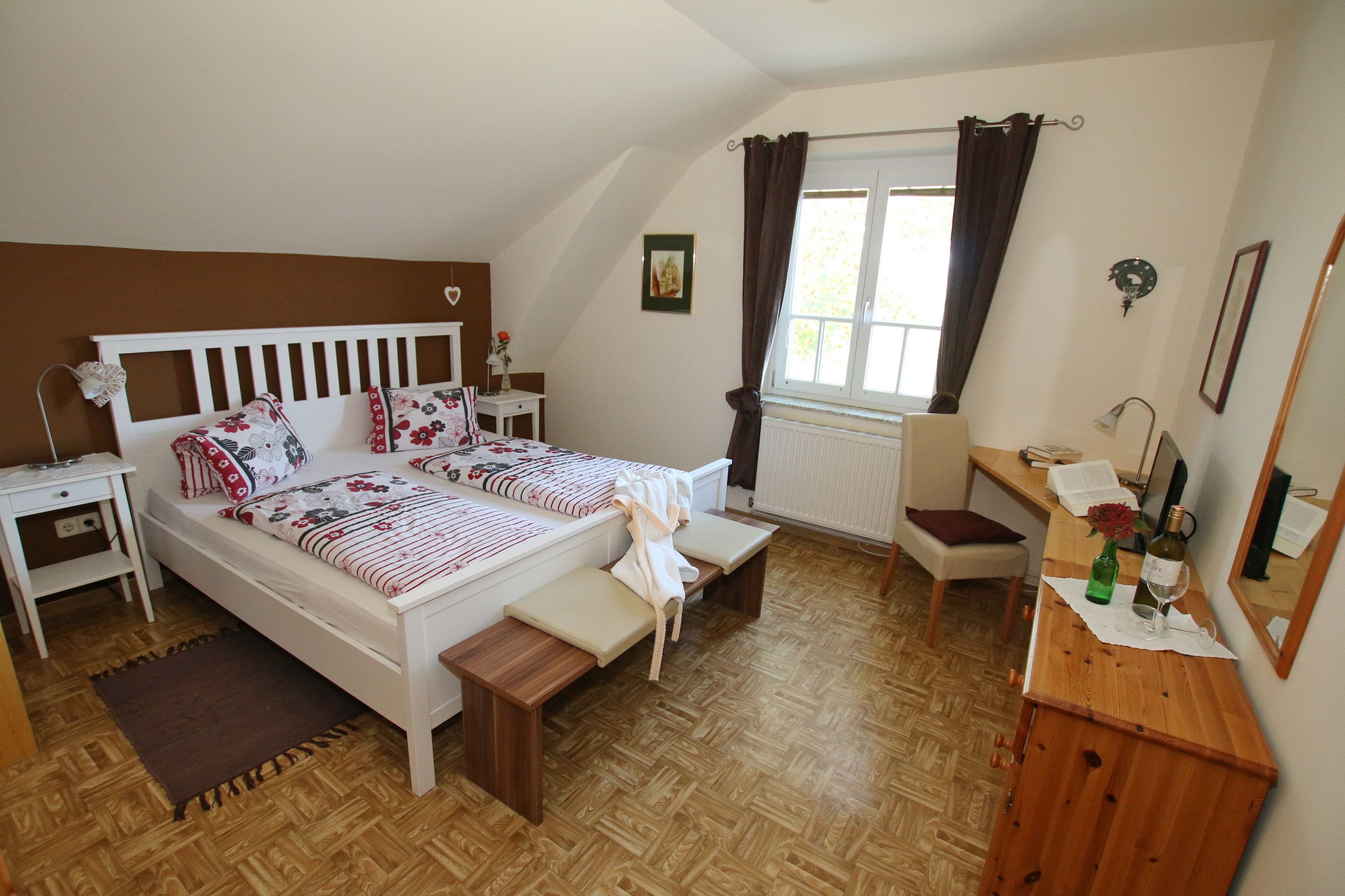 Cozy guest room with double bed, sofa, table and chair. Brown accent wall and dark curtains.