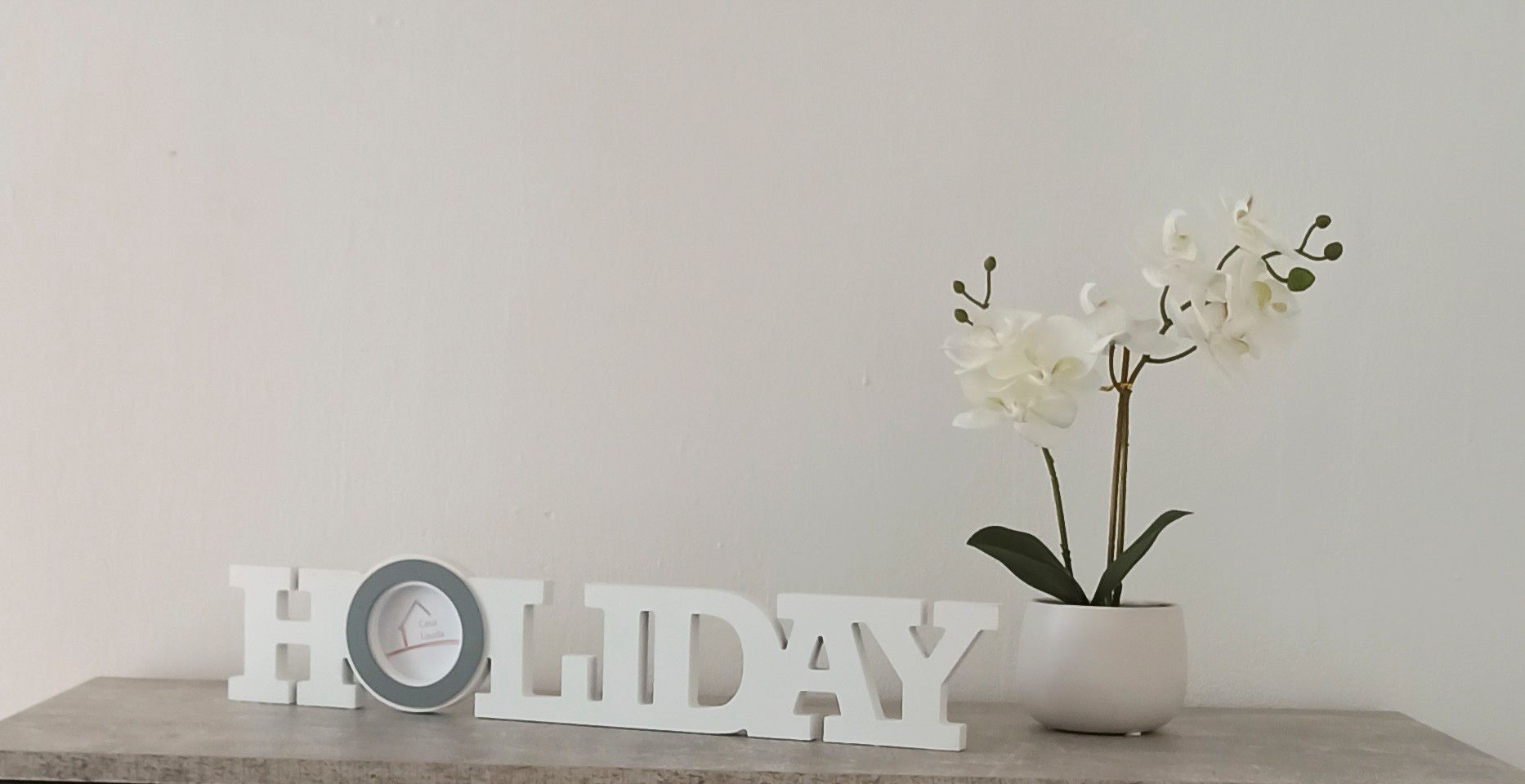 Decoration with 'HOLIDAY' lettering and white orchid in a pot on a table.