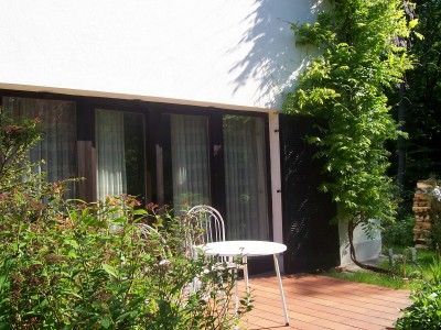 Terrace with table and chair in front of a house with large windows.