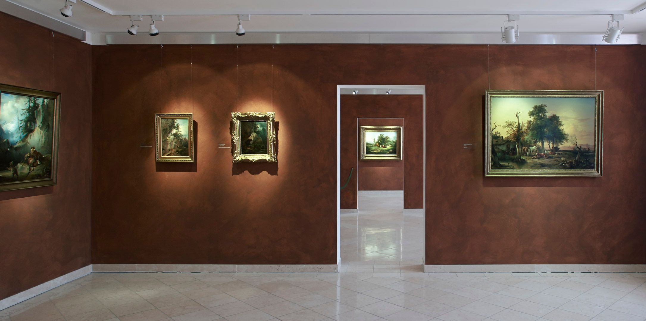Interior view of a museum with paintings on brown walls.