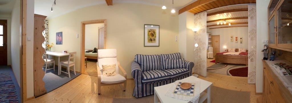 Panorama of a cozy living room with sofa, dining table and bedroom in the background.