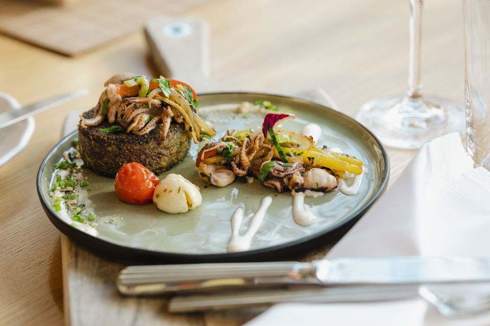 Gourmet dish on a plate with vegetables and seafood, decoratively arranged.