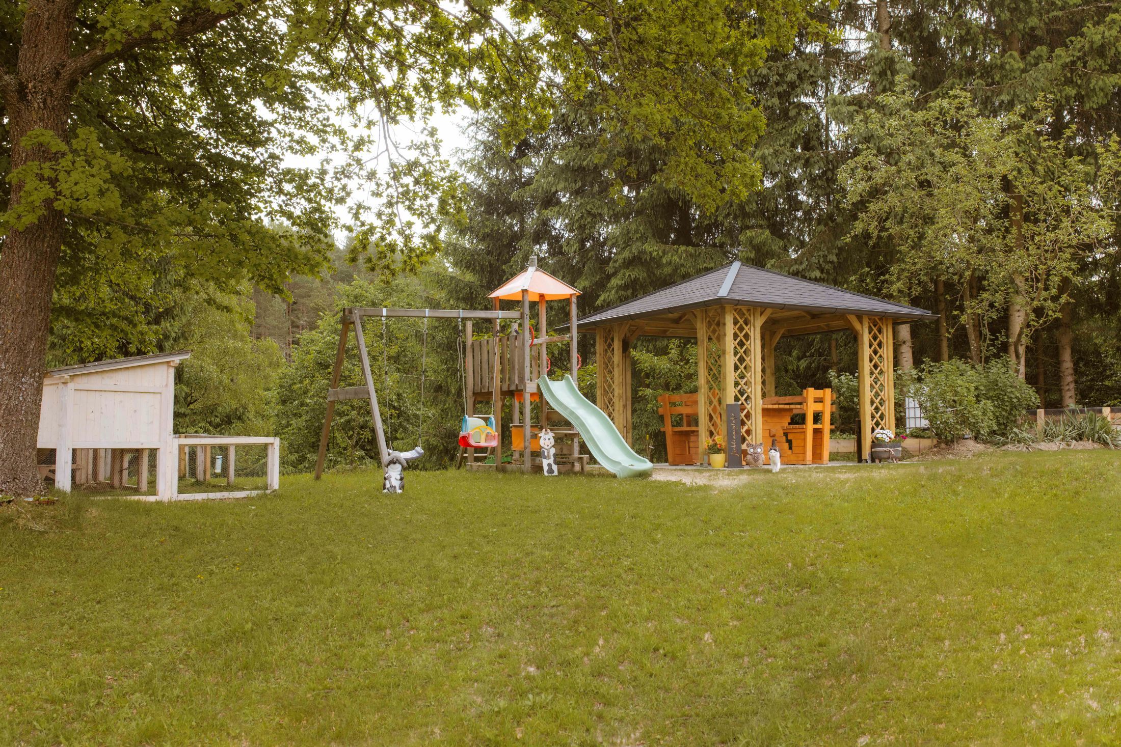 A playground with swings, slide and pavilion in a green garden.