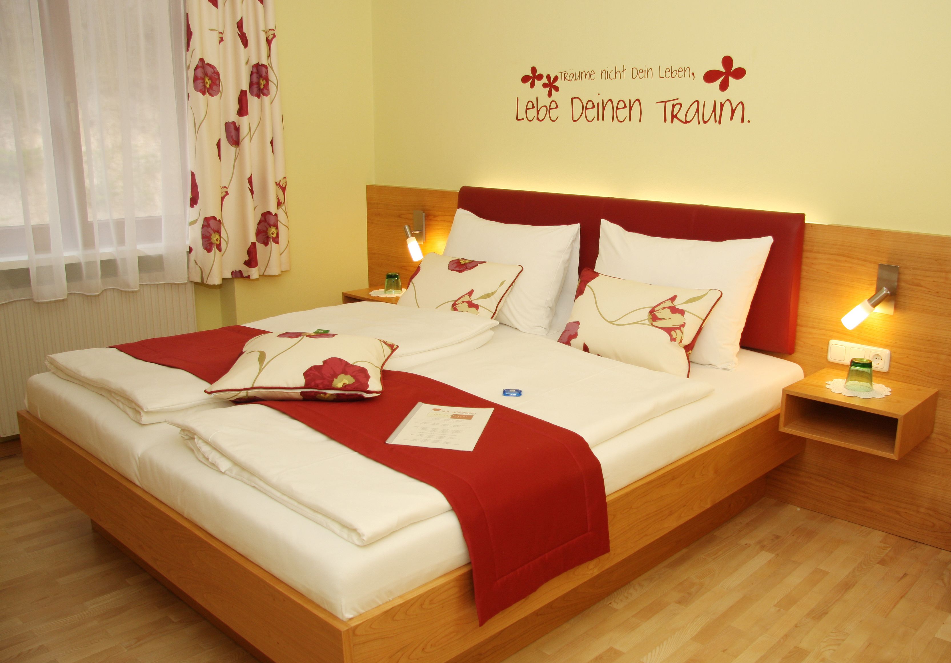A cozy hotel room with a double bed, red accents and an inspiring wall quote.