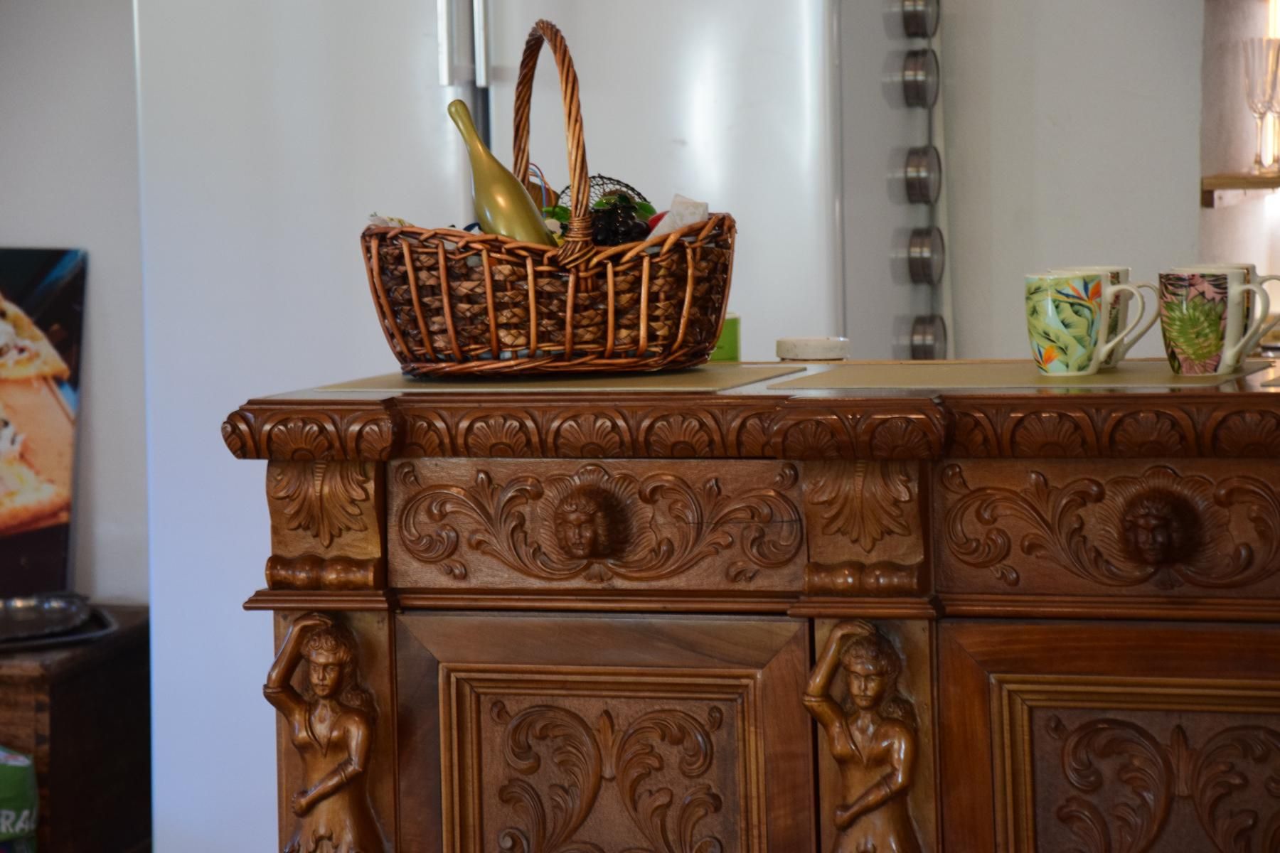 A carved wooden buffet with a basket and cups on top.