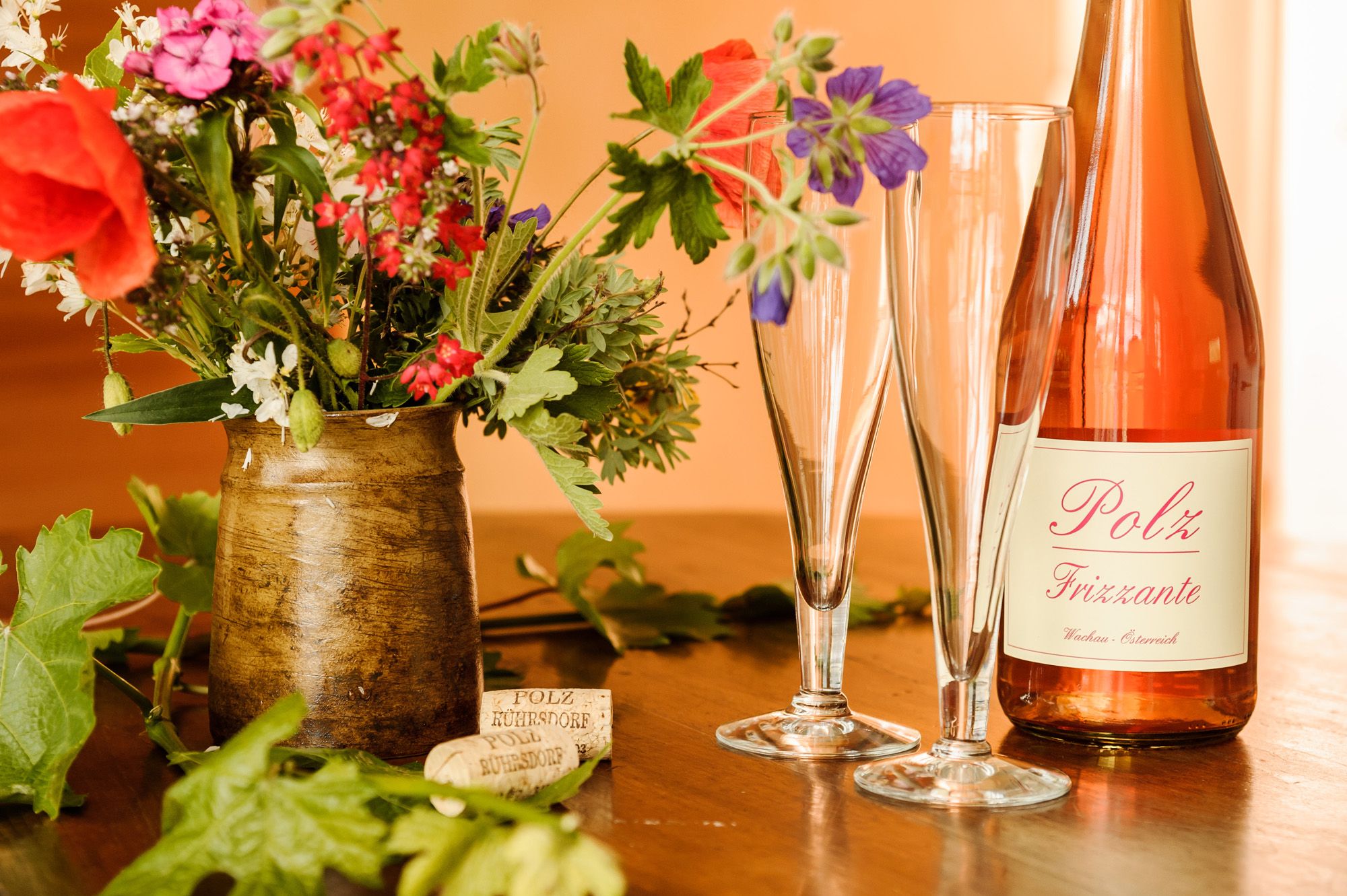 A bottle of Polz Frizzante with two glasses and a bouquet of flowers on a table.