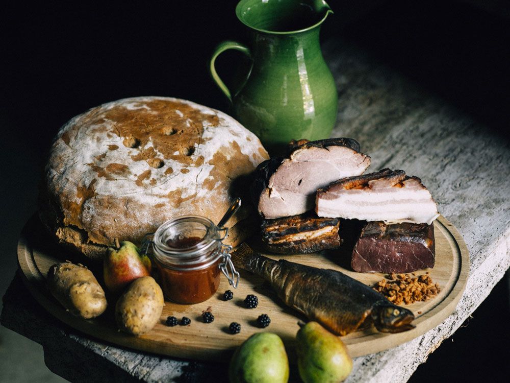 A rustic arrangement with bread, meat, fish, pears, potatoes and jam on a wooden table.