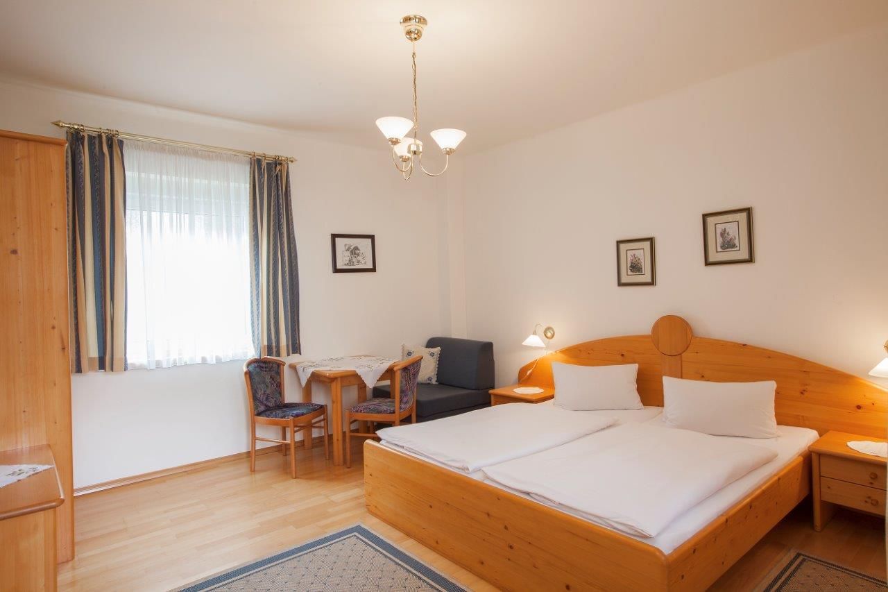 A cozy hotel room with a double bed, wooden furniture and a small table with chairs.