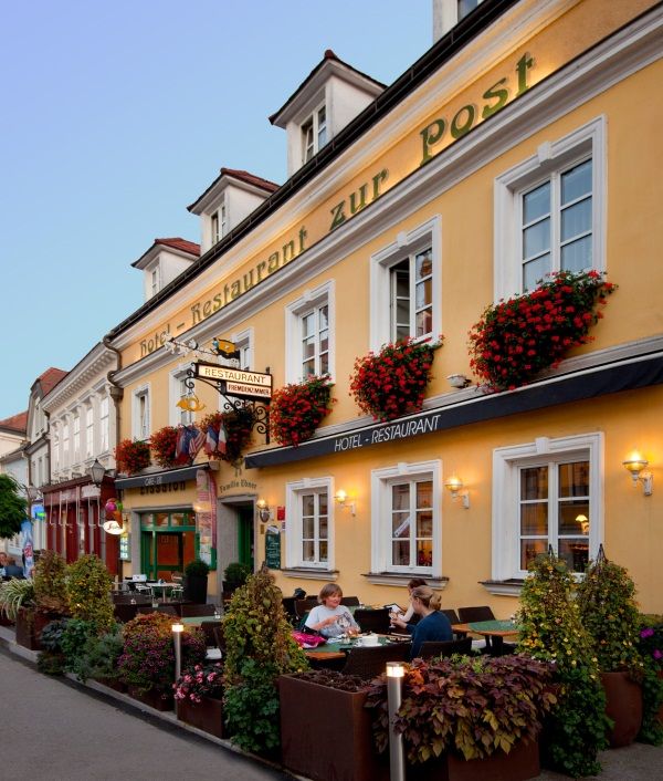 Facade of a yellow building with the lettering 'Hotel-Restaurant zur Post'. People are sitting at tables in front of the building.