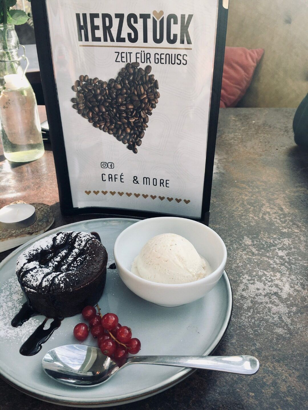 A dessert plate with chocolate cake, vanilla ice cream and currants next to a centerpiece menu.