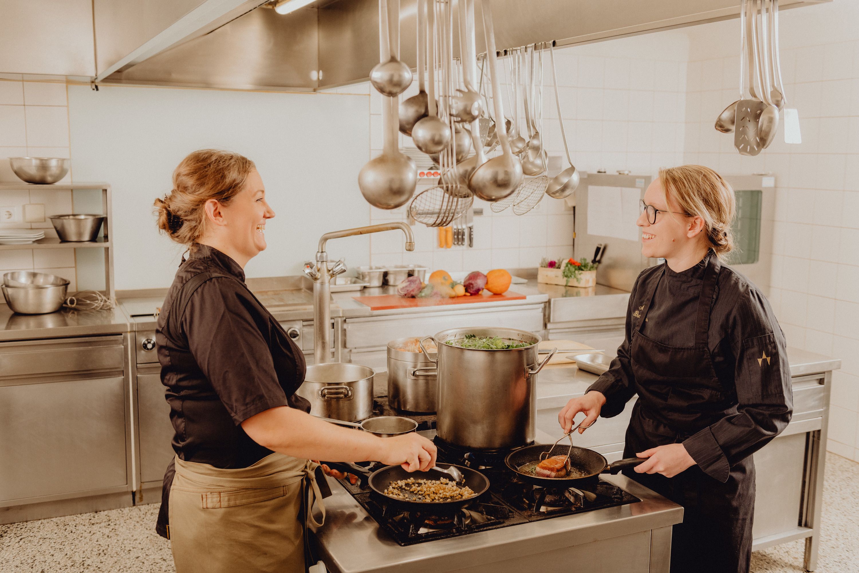 Two cooks in a professional kitchen working at a stove.