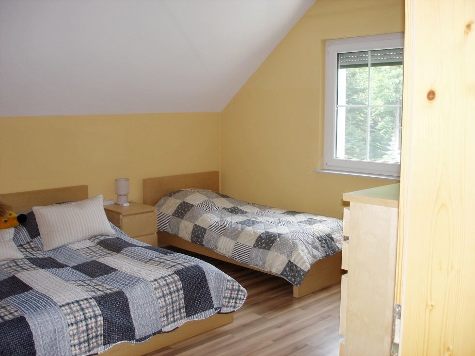 Two single beds in a yellow-painted bedroom with sloping ceiling and window.