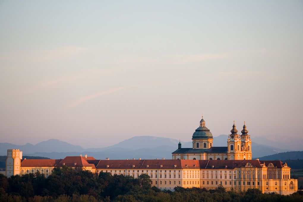 Melk Abbey in Austria at sunset with mountains in the background.