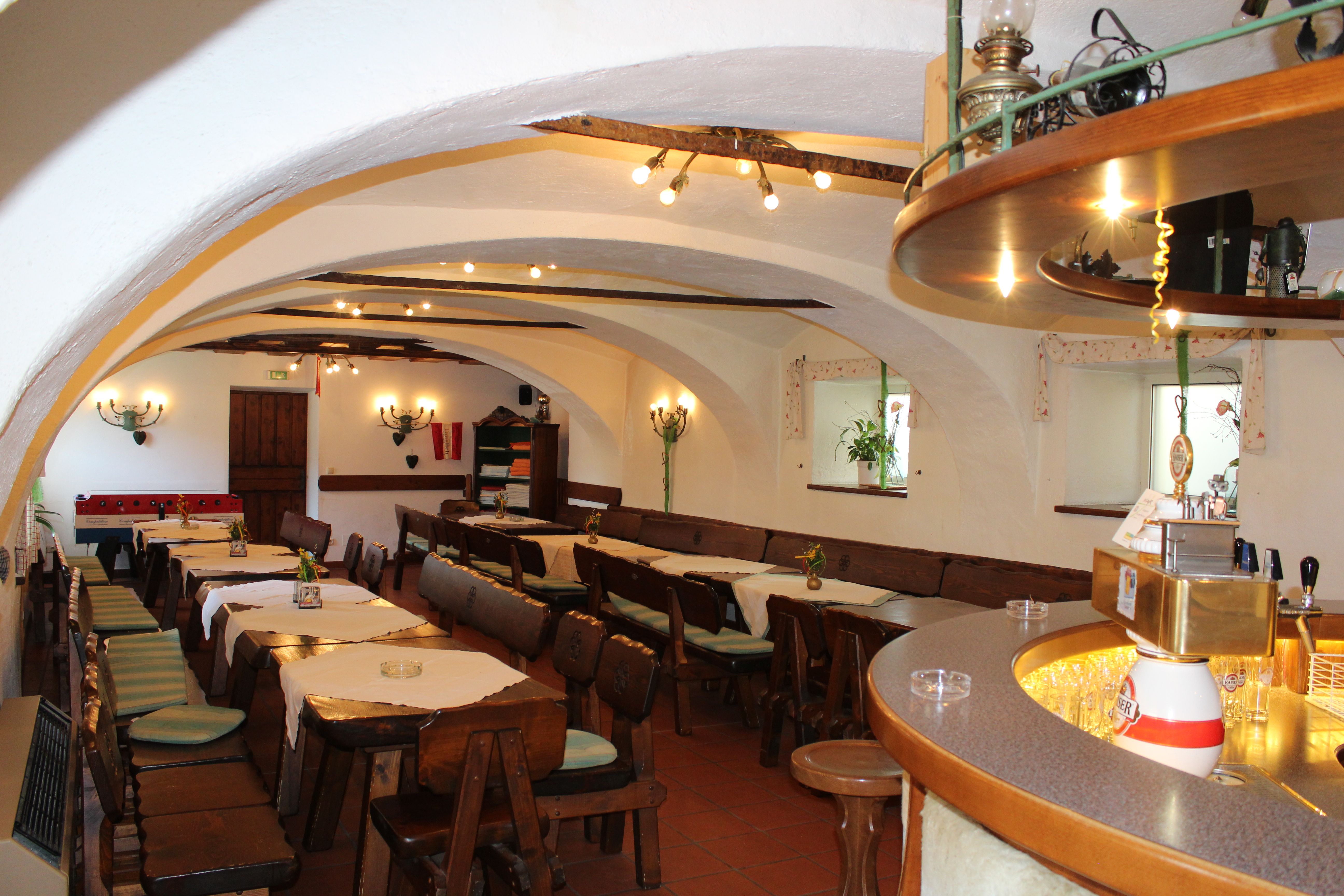 Interior view of a rustic bar with wooden tables and chairs, vaulted ceiling and counter.