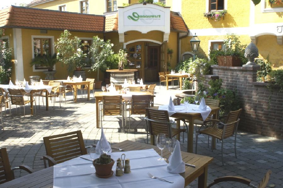 Outdoor area of the DONAUWIRT Hotel with laid tables and plants.
