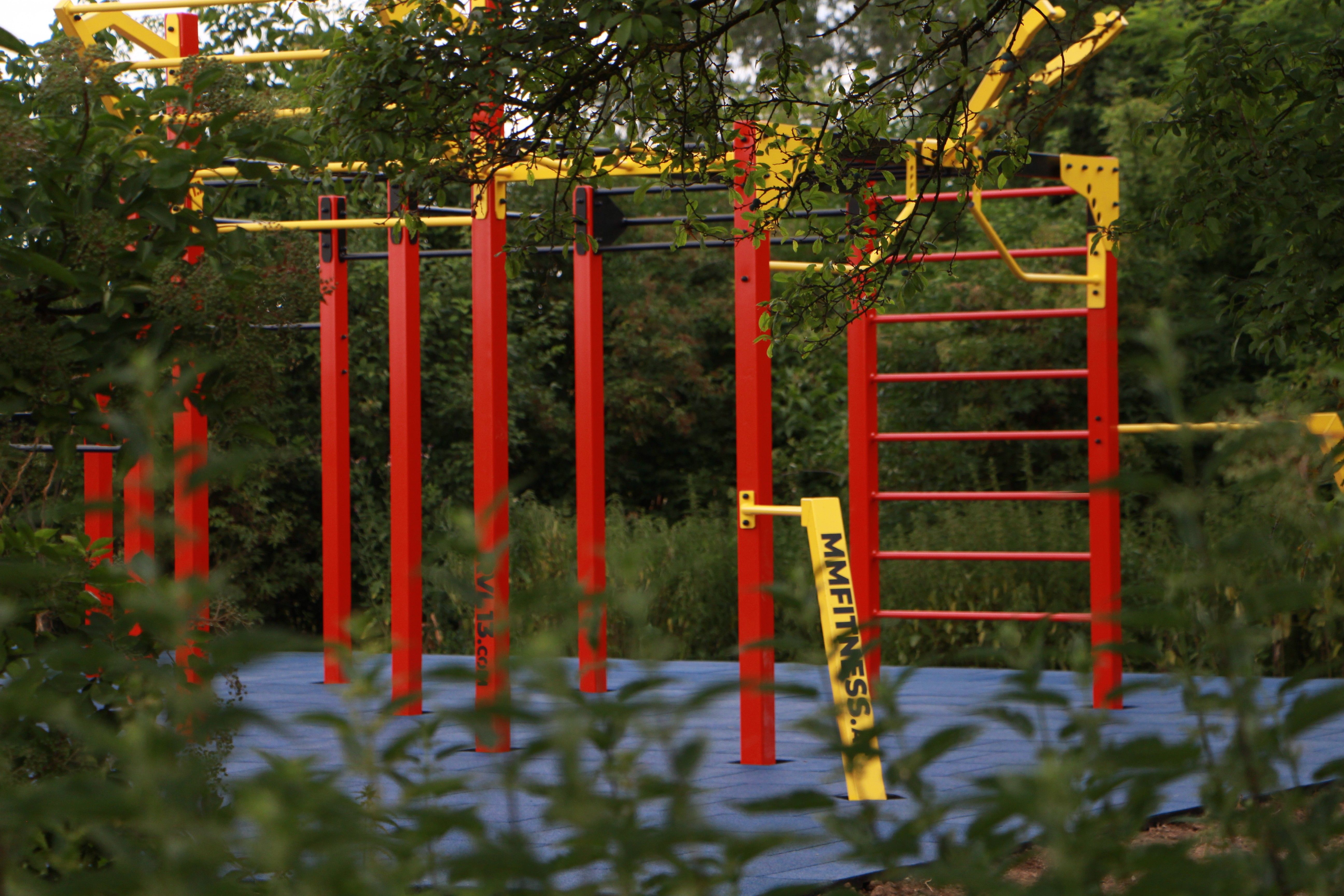 A calisthenics park with red and yellow poles surrounded by green vegetation.