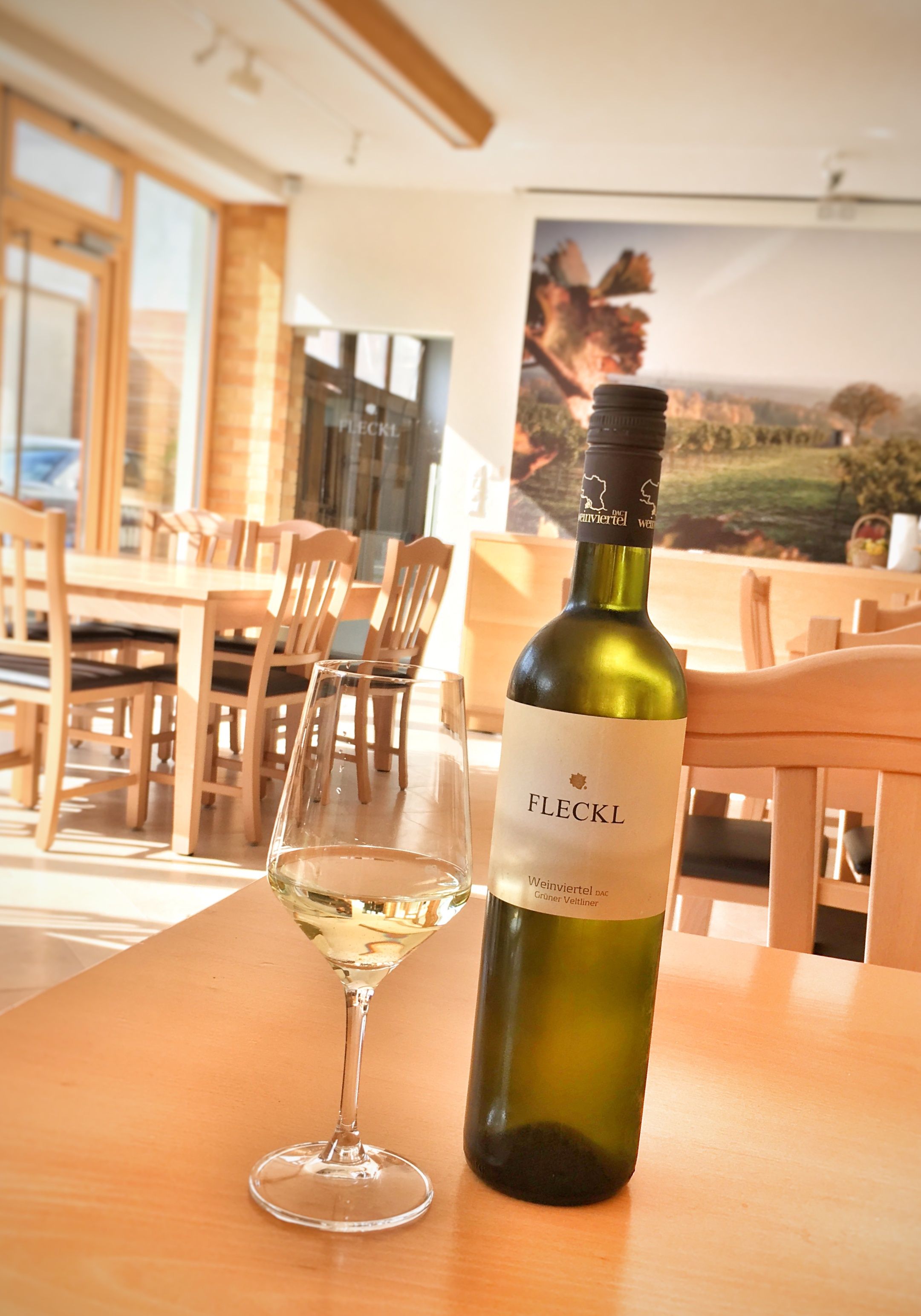 A bottle of white wine and a filled wine glass on a wooden table in a tasting room.