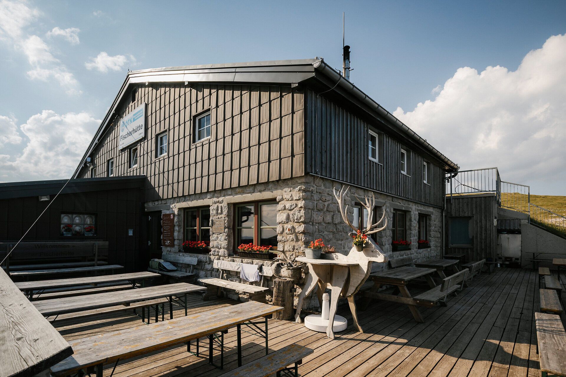 A fisherman's cabin on Schneeberg with a terrace, benches, and a decorative ibex statue in front of the building