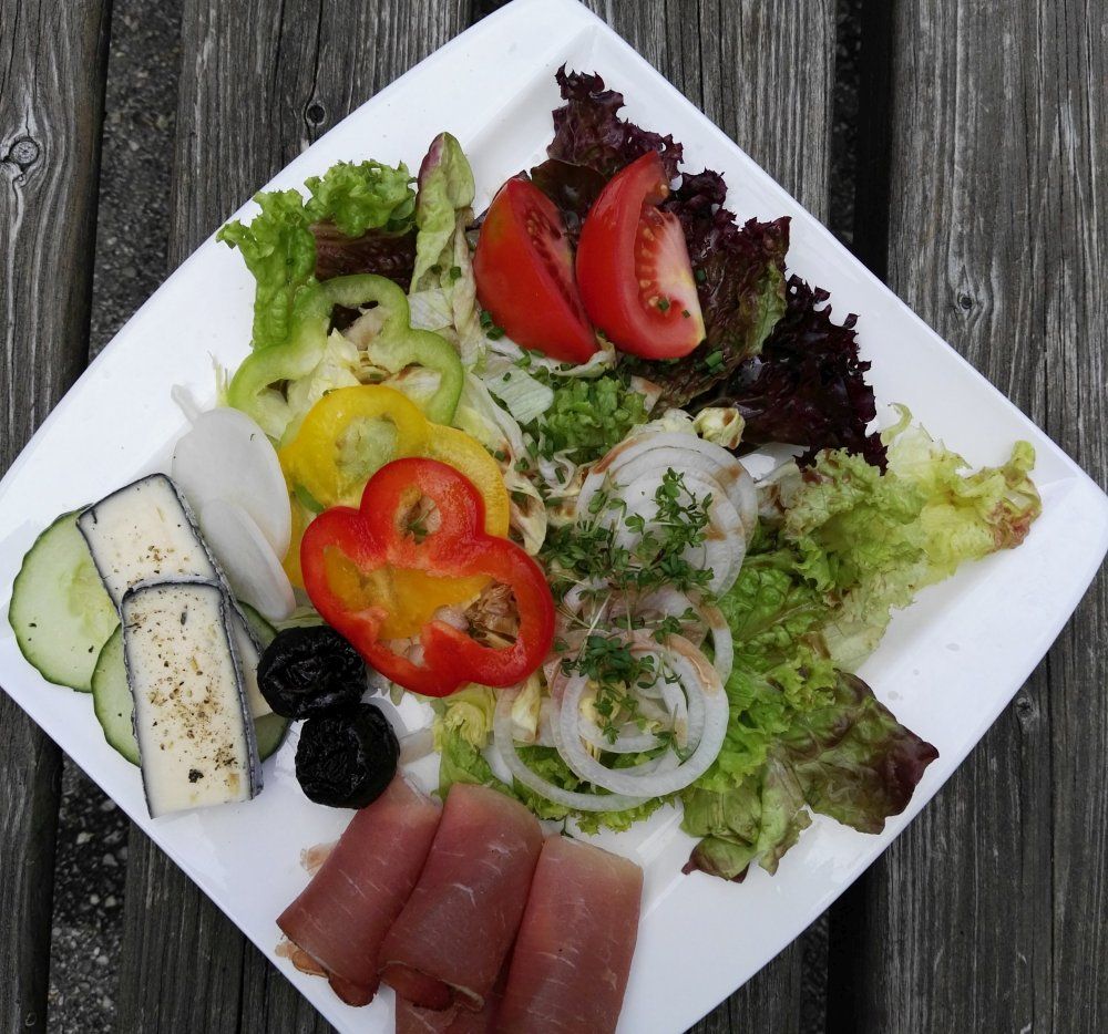 A plate of lettuce, tomatoes, peppers, onions, ham and cheese on a wooden table.