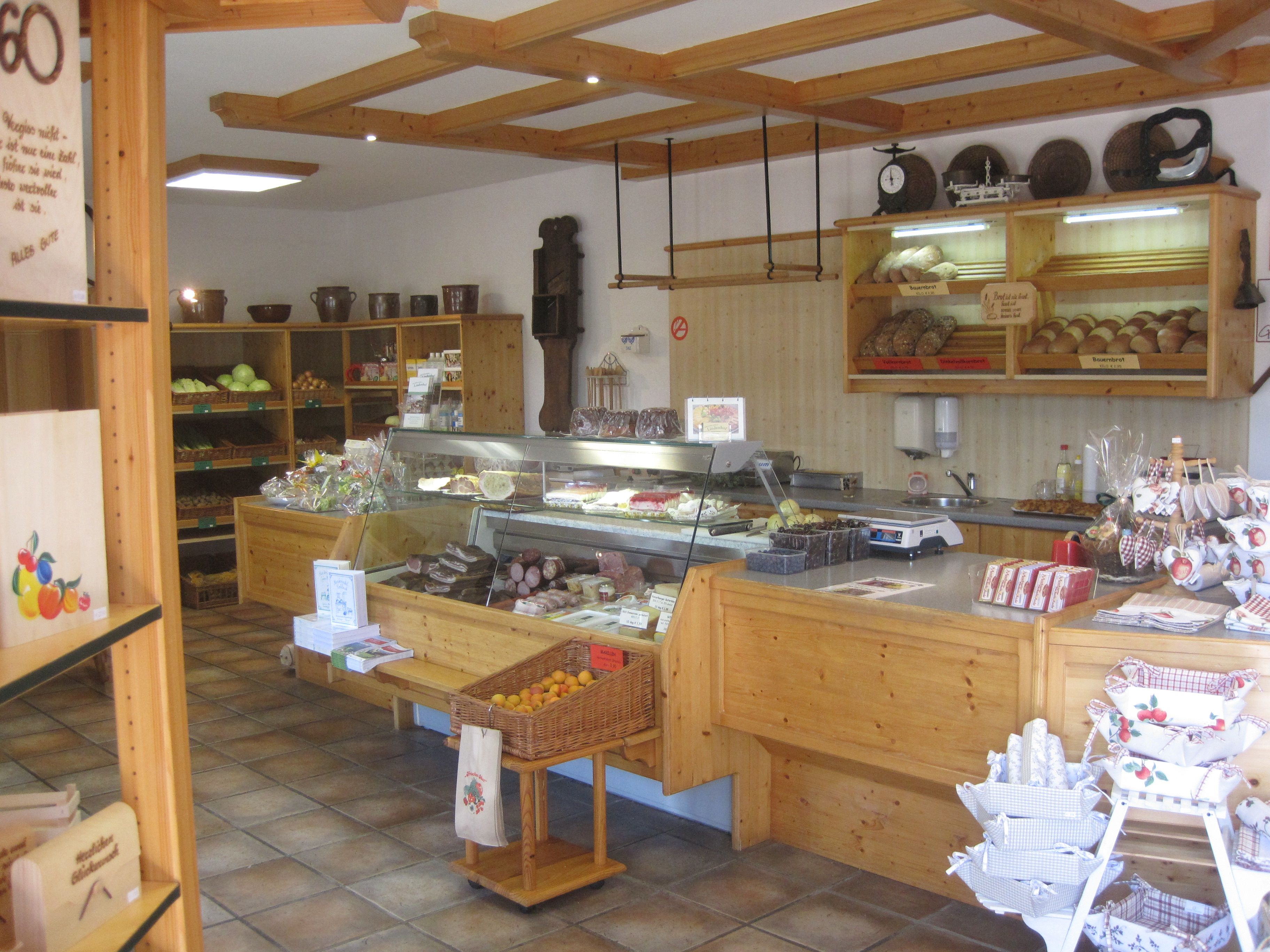 Interior view of a farm store with wooden shelves filled with bread, fruit and sausage products.