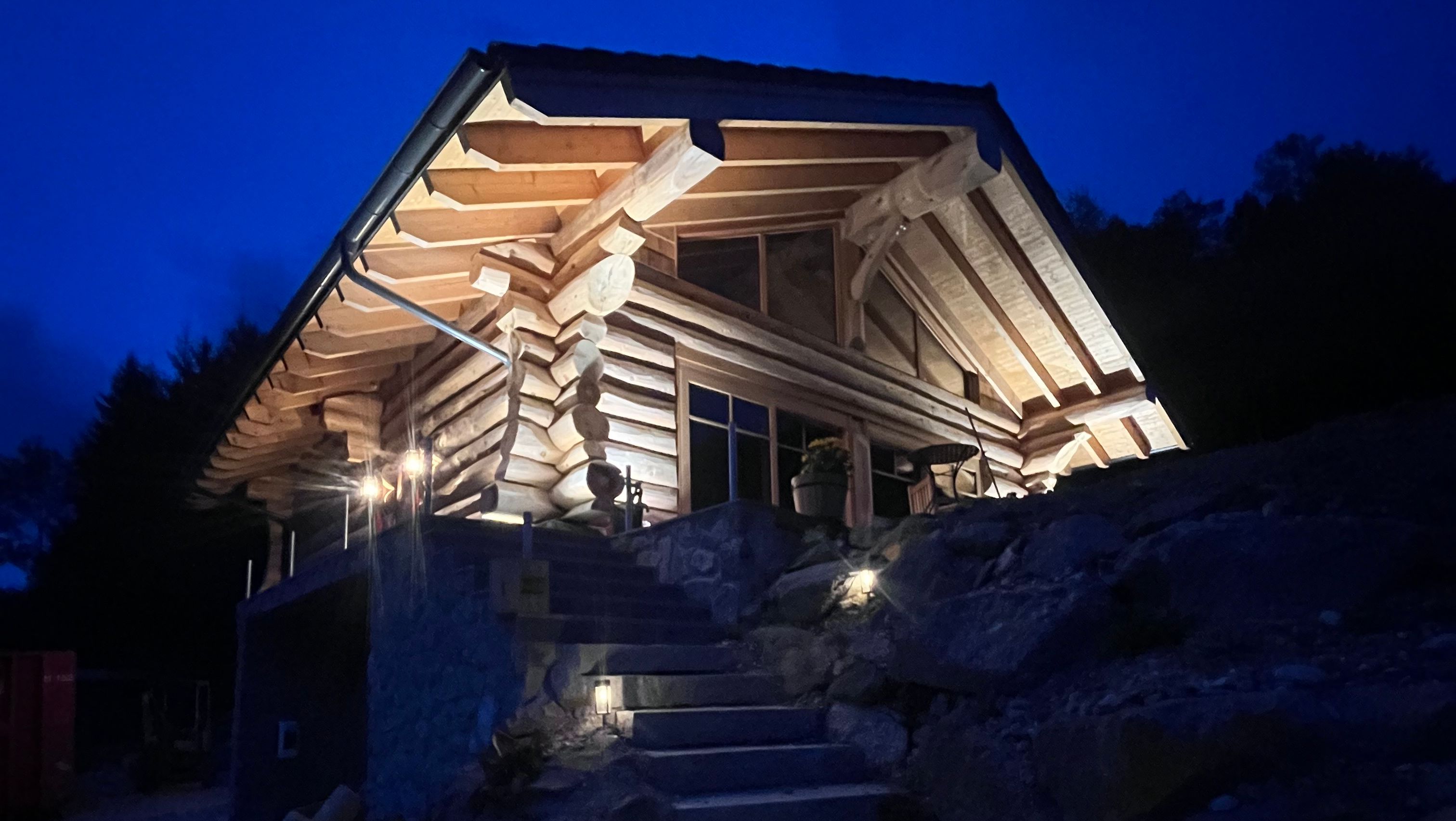 An illuminated wooden chalet at night with stone steps in the foreground.