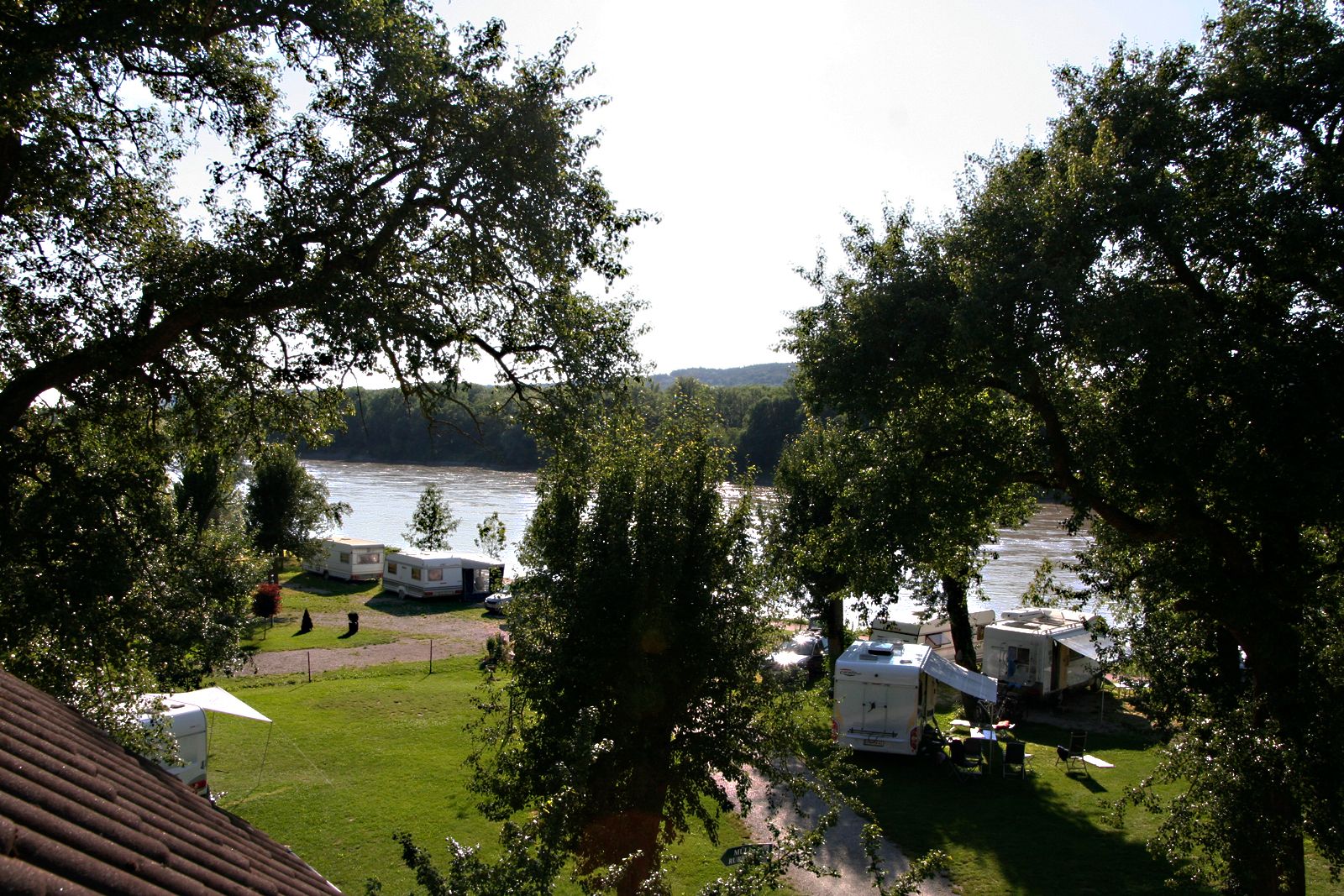 Campsite by the river with caravans and trees.