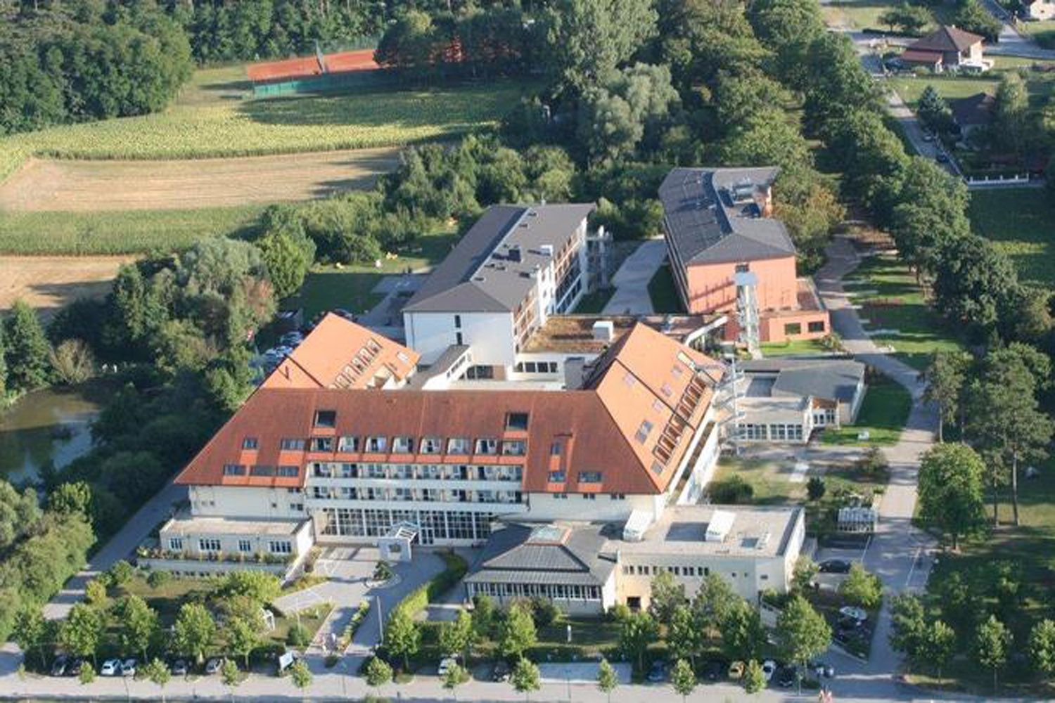 Aerial view of a clinic with red roofs, surrounded by trees and fields.