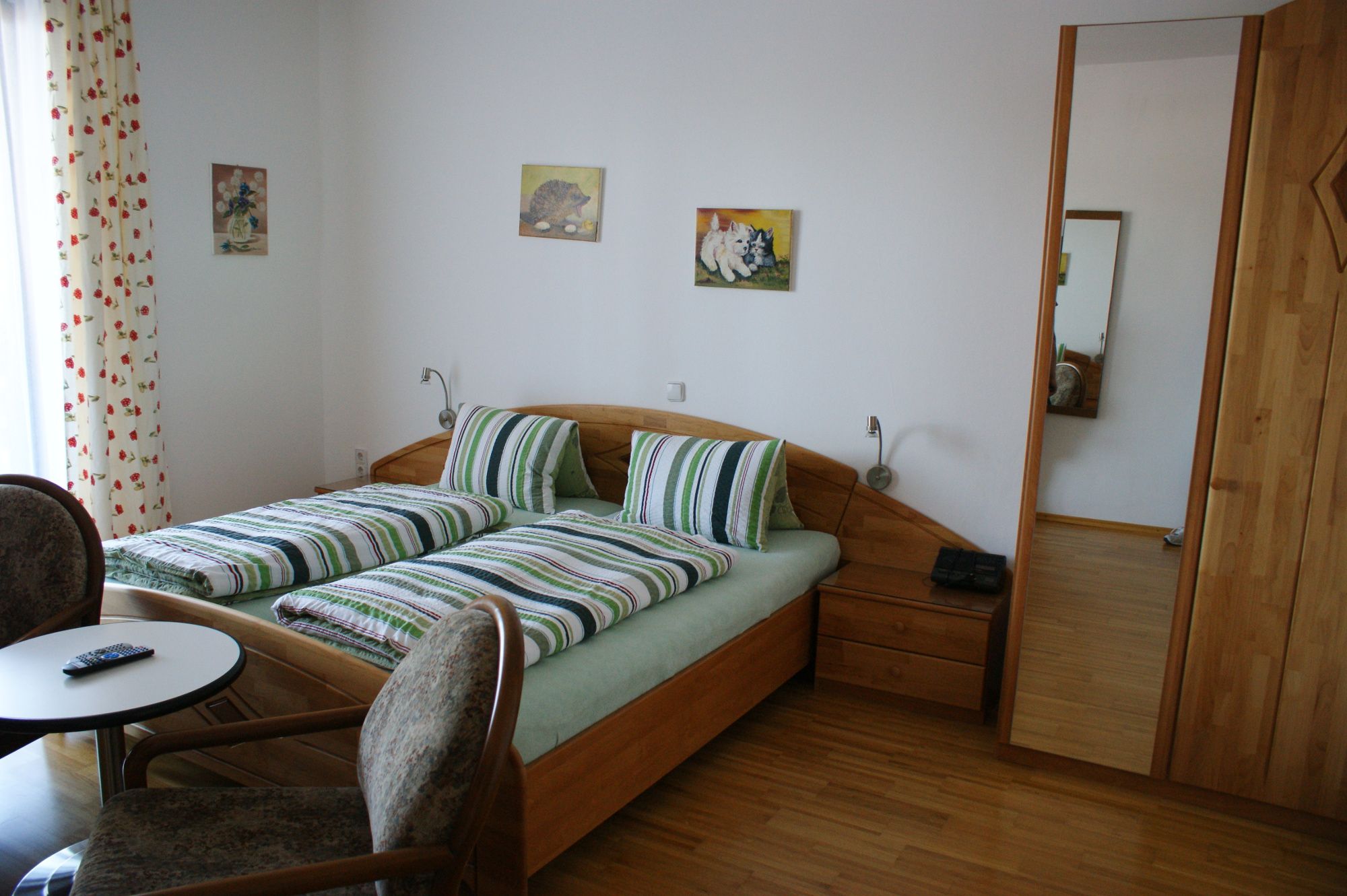 A cozy bedroom with a double bed, striped bed linen, two chairs and a small table. There are pictures on the wall.